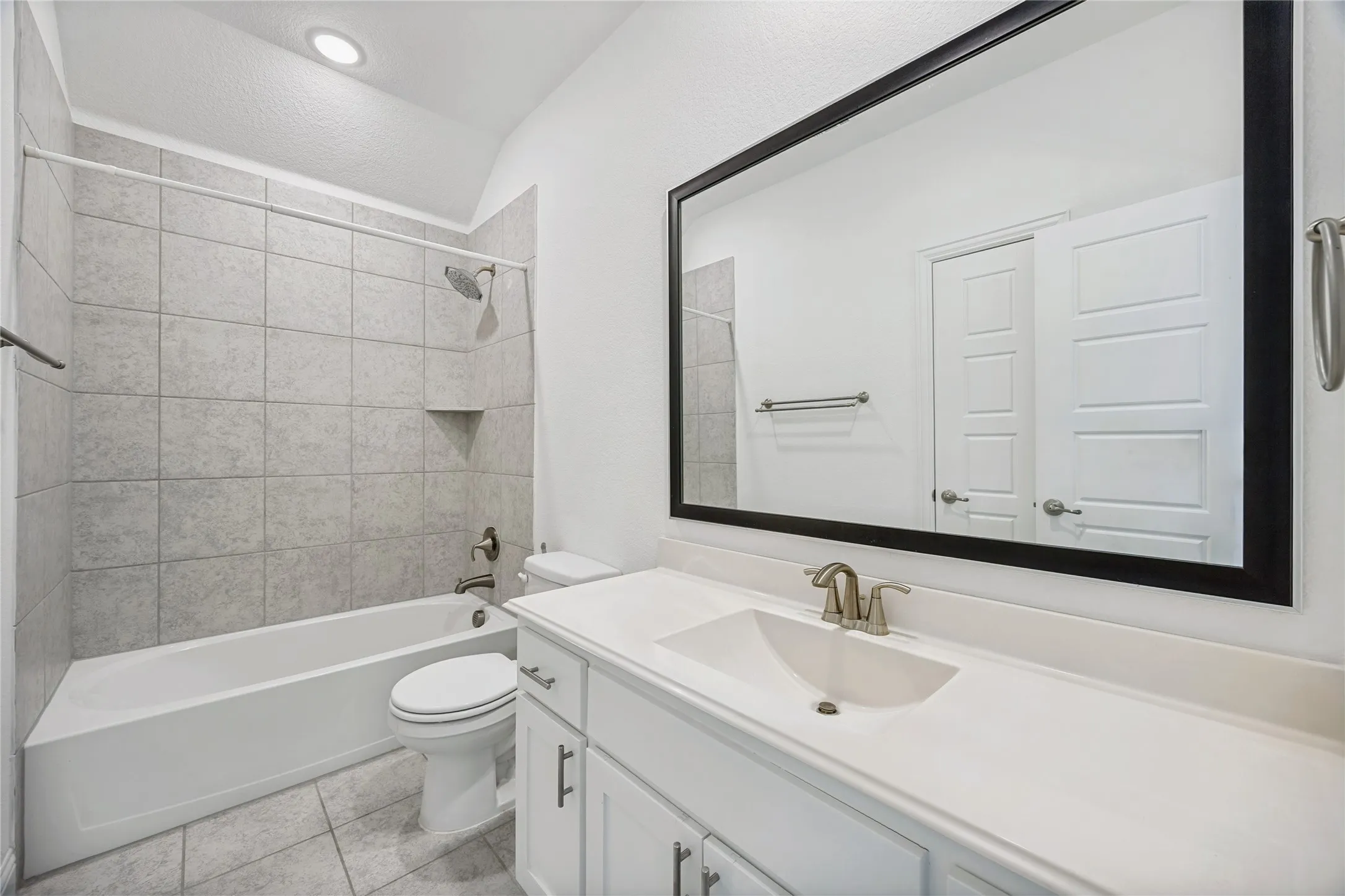 Full bathroom featuring a white vanity with an integrated sink, a large framed mirror, and a tub-shower combination with tiled surround and built-in niche