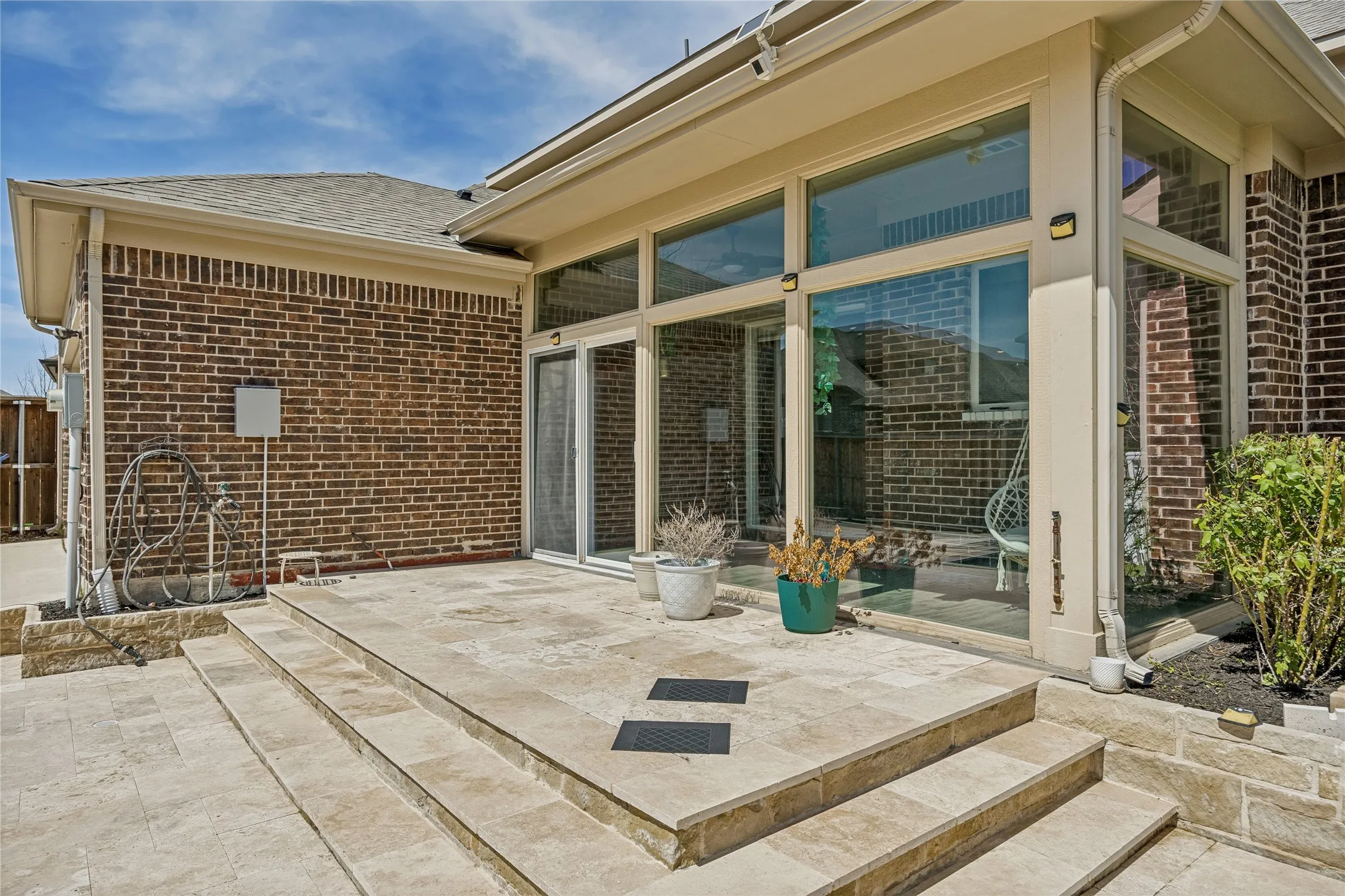 Multi-level stone patio featuring a brick exterior and a full-glass sunroom with a sliding door