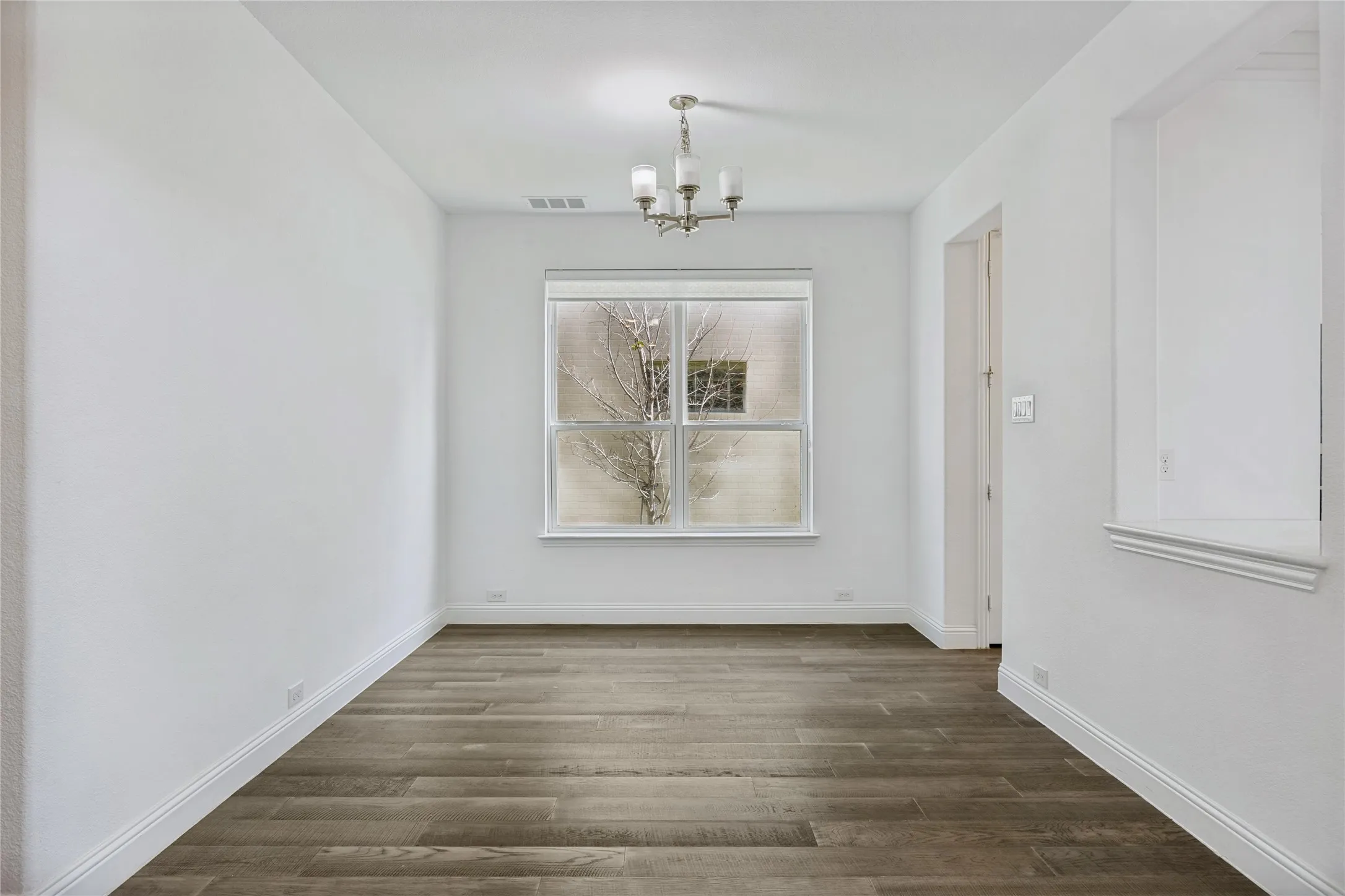 Bright room featuring wood-finish flooring, white baseboards, a central window, recessed wall niche, and a brushed nickel chandelier