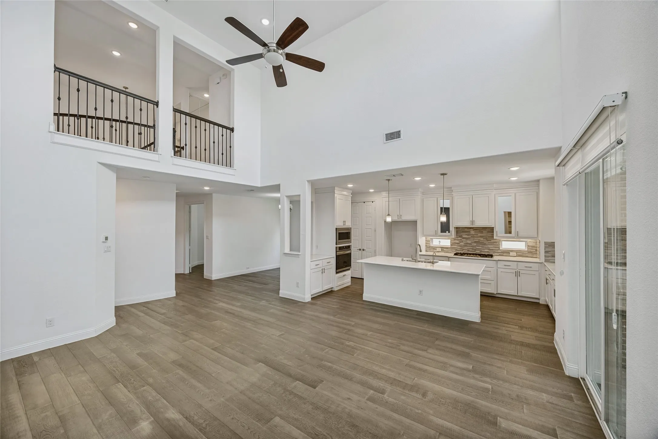 Open-concept living area featuring high ceilings with a ceiling fan, wood-finish flooring, and a kitchen with white cabinetry, a large island, and stainless steel appliances