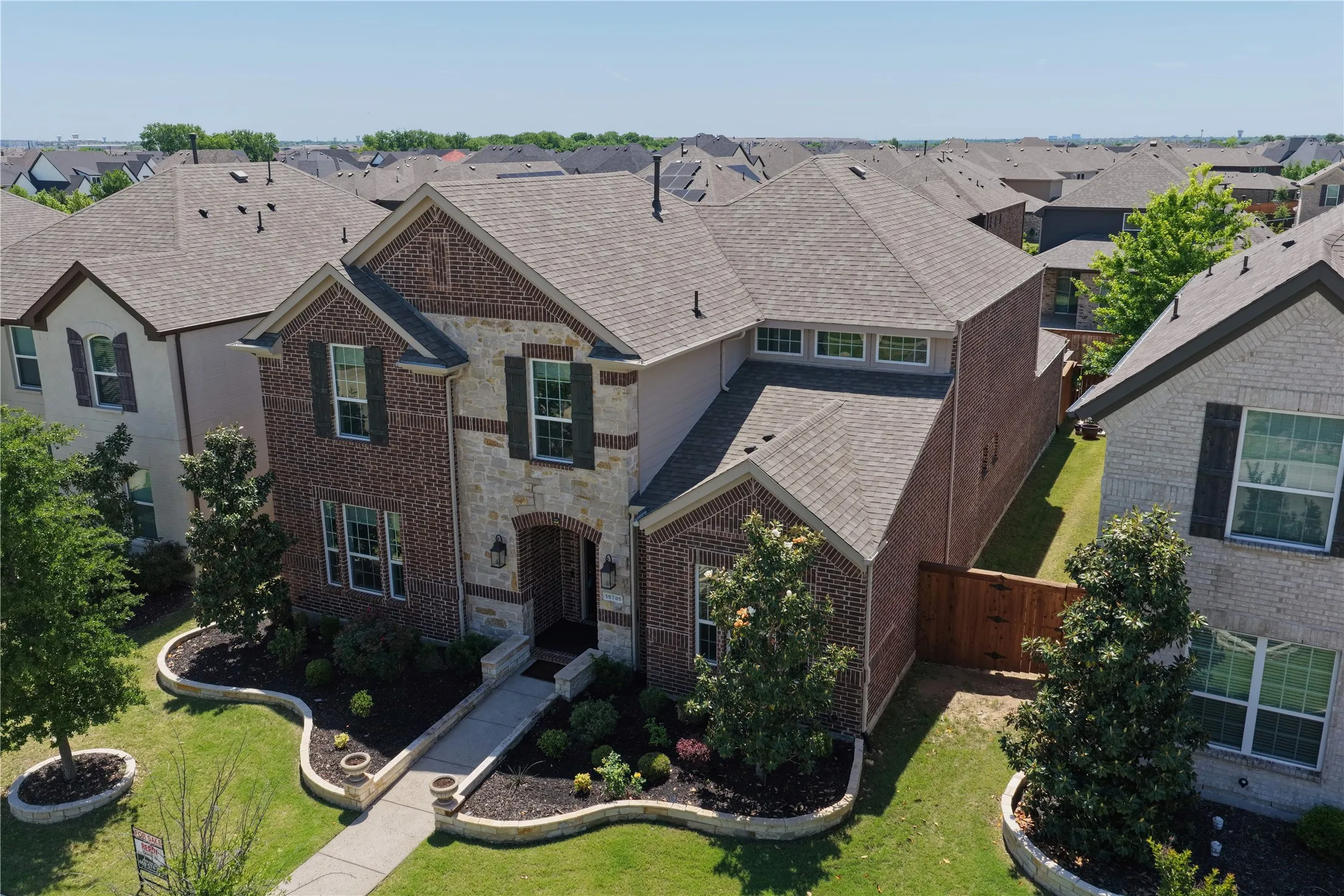 Two-story residential property featuring a brick and stone facade, dark shutters, and a gray shingle roof