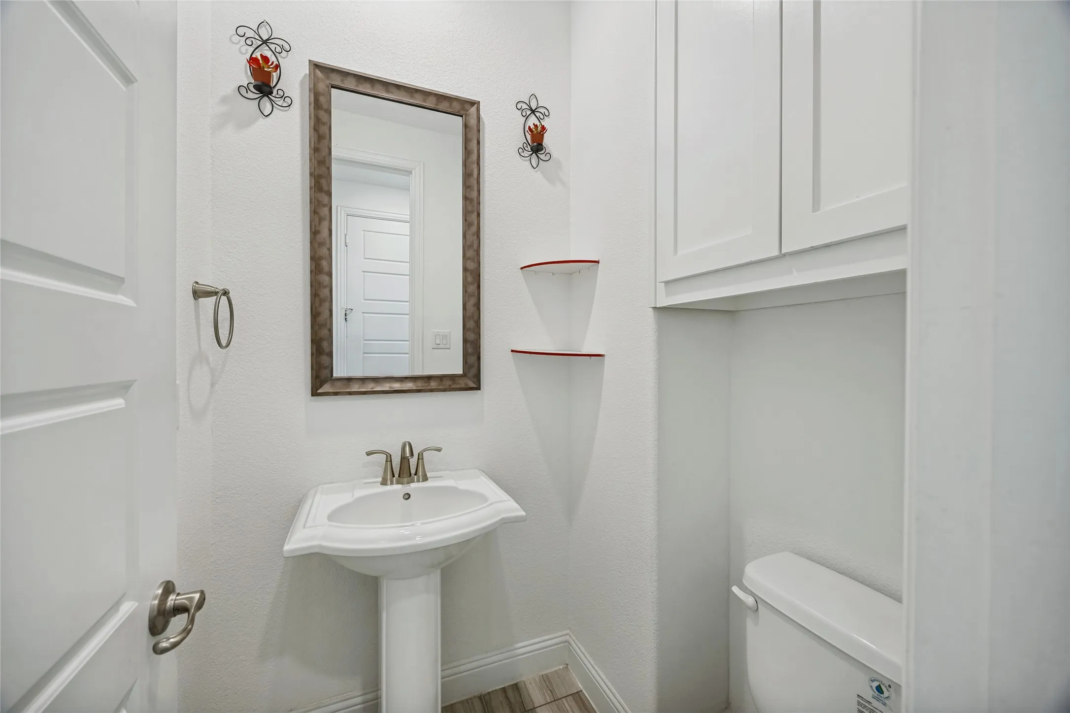 Well-appointed powder room featuring a pedestal sink with chrome-finish faucet, a framed mirror, and wood-finish flooring