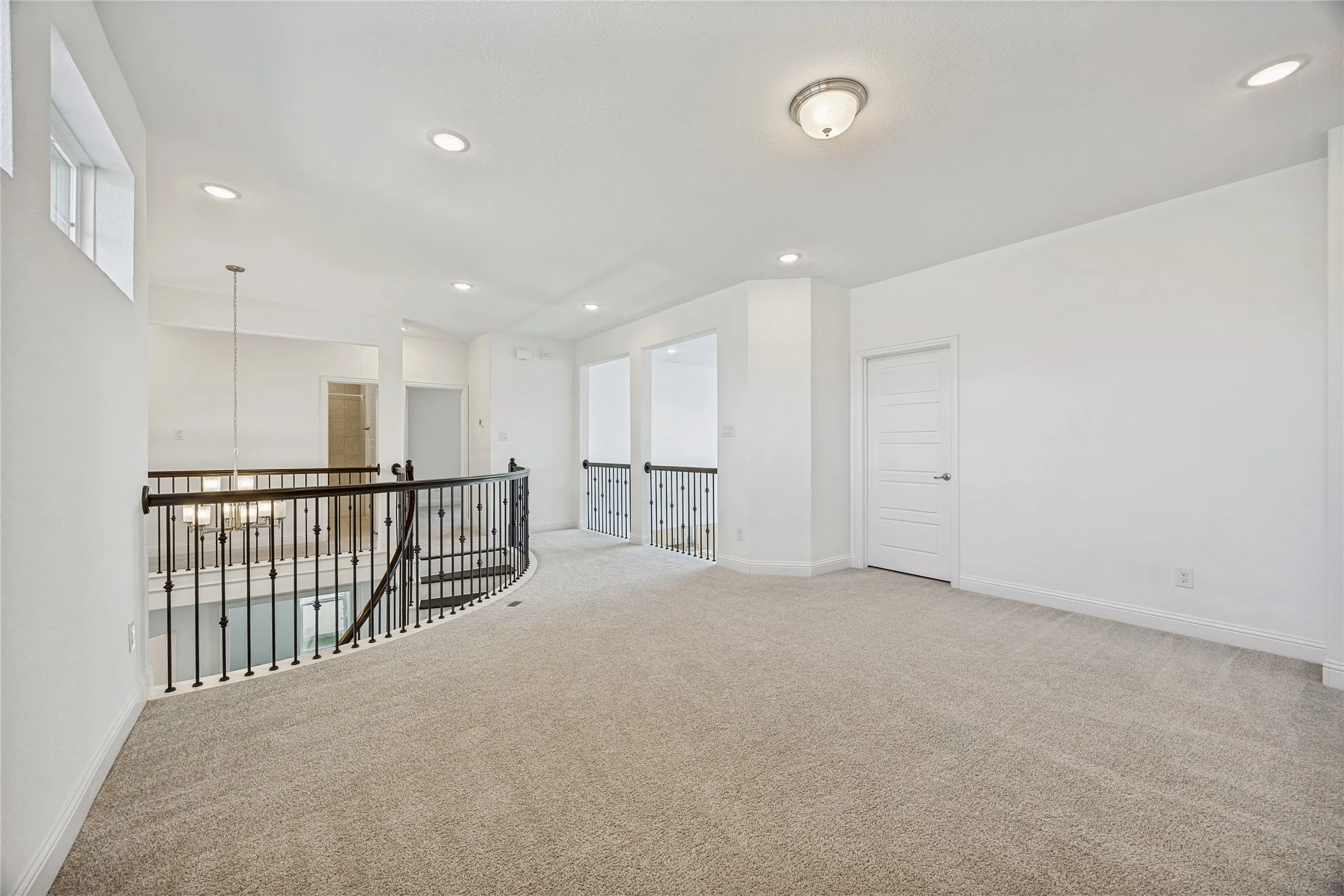 Upper level landing featuring light beige carpet, white walls, recessed lighting, and an ornate wrought iron railing