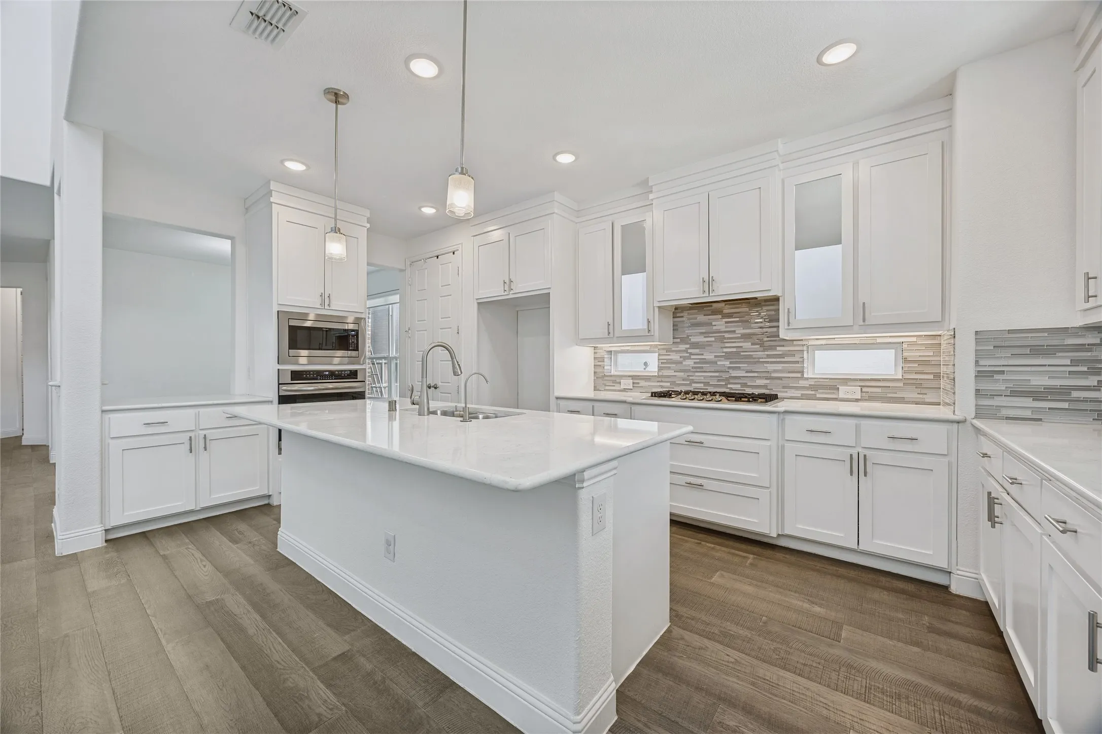 Bright kitchen featuring white shaker cabinetry, an expansive center island with a sink, recessed lighting, stainless steel appliances, and wood-finish flooring