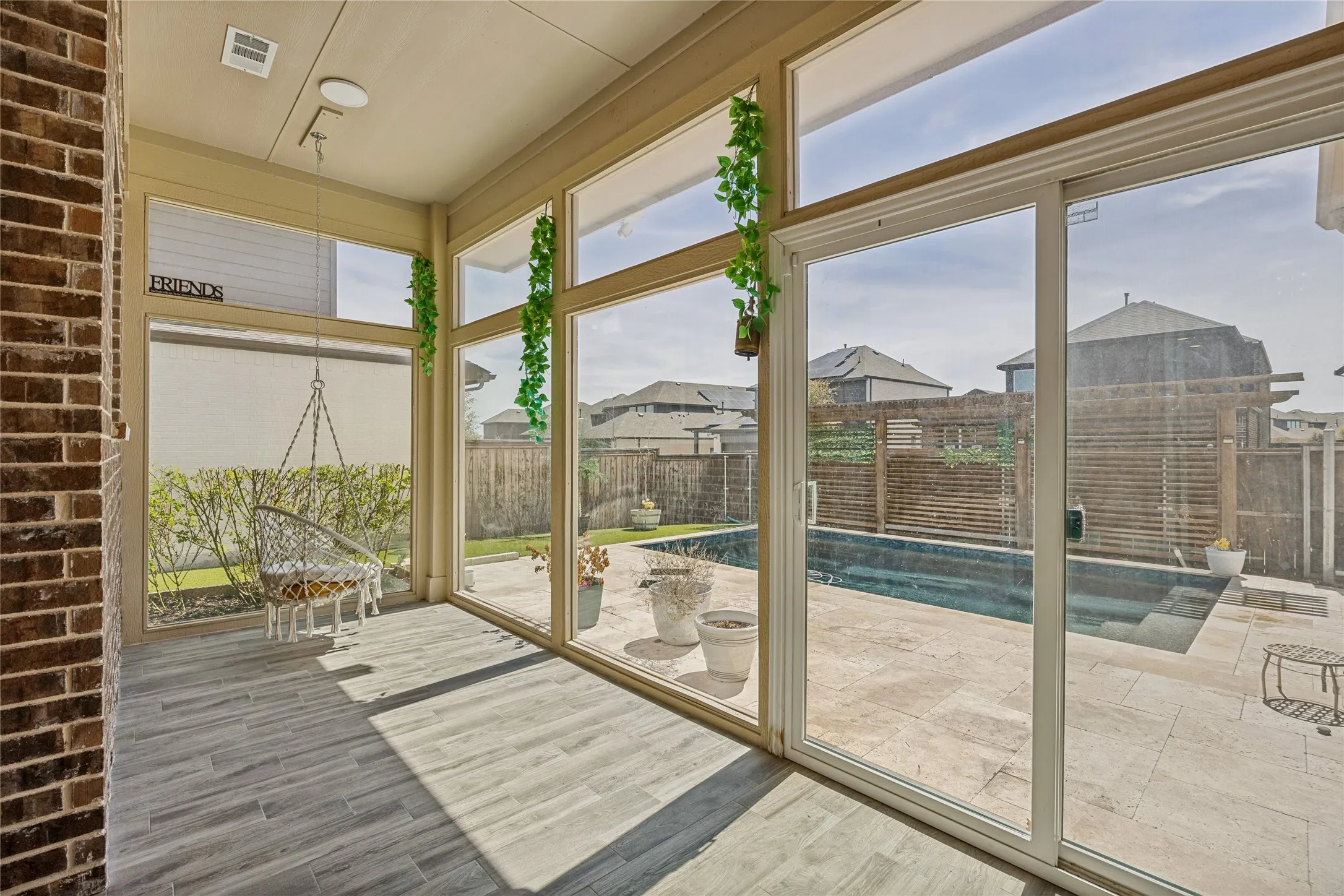Sunroom featuring wood-finish tile flooring, a brick accent wall, and expansive windows