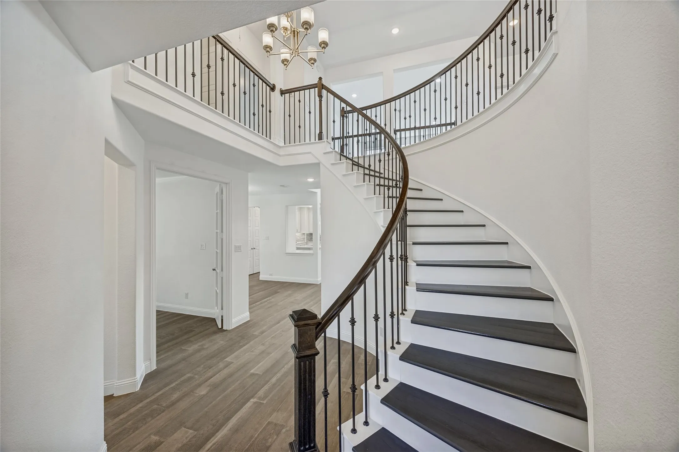 Grand curved staircase with dark treads and white risers, featuring an ornate wrought iron railing