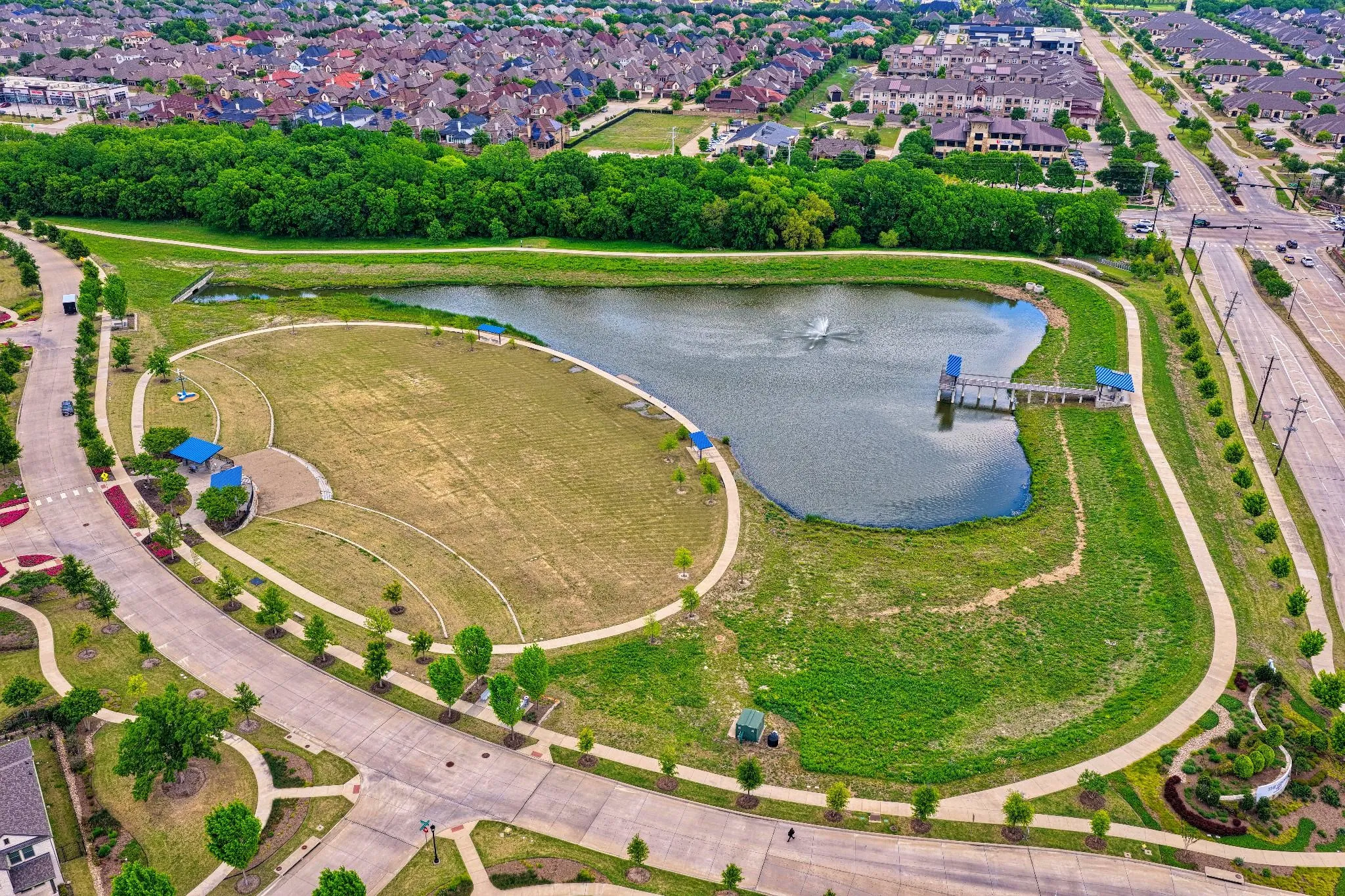 Expansive park area featuring a central pond with a fountain, a pier structure with covered sections, extensive walking paths, and green spaces