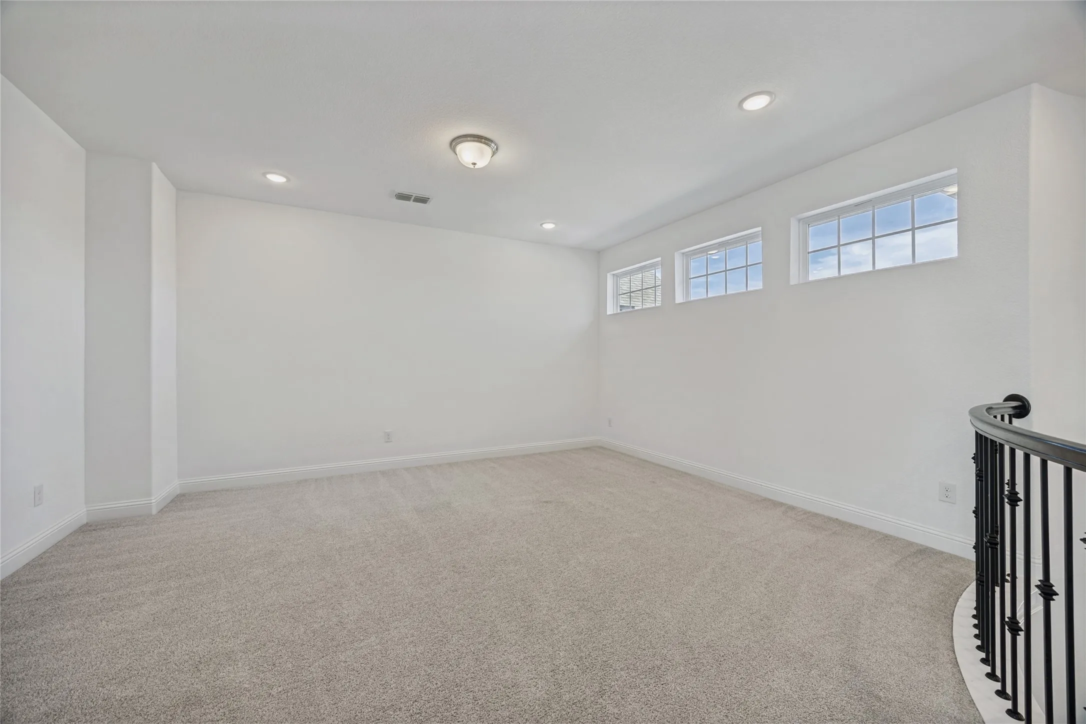 Spacious room featuring neutral carpeting and white walls, illuminated by recessed lighting and a central flush-mount fixture