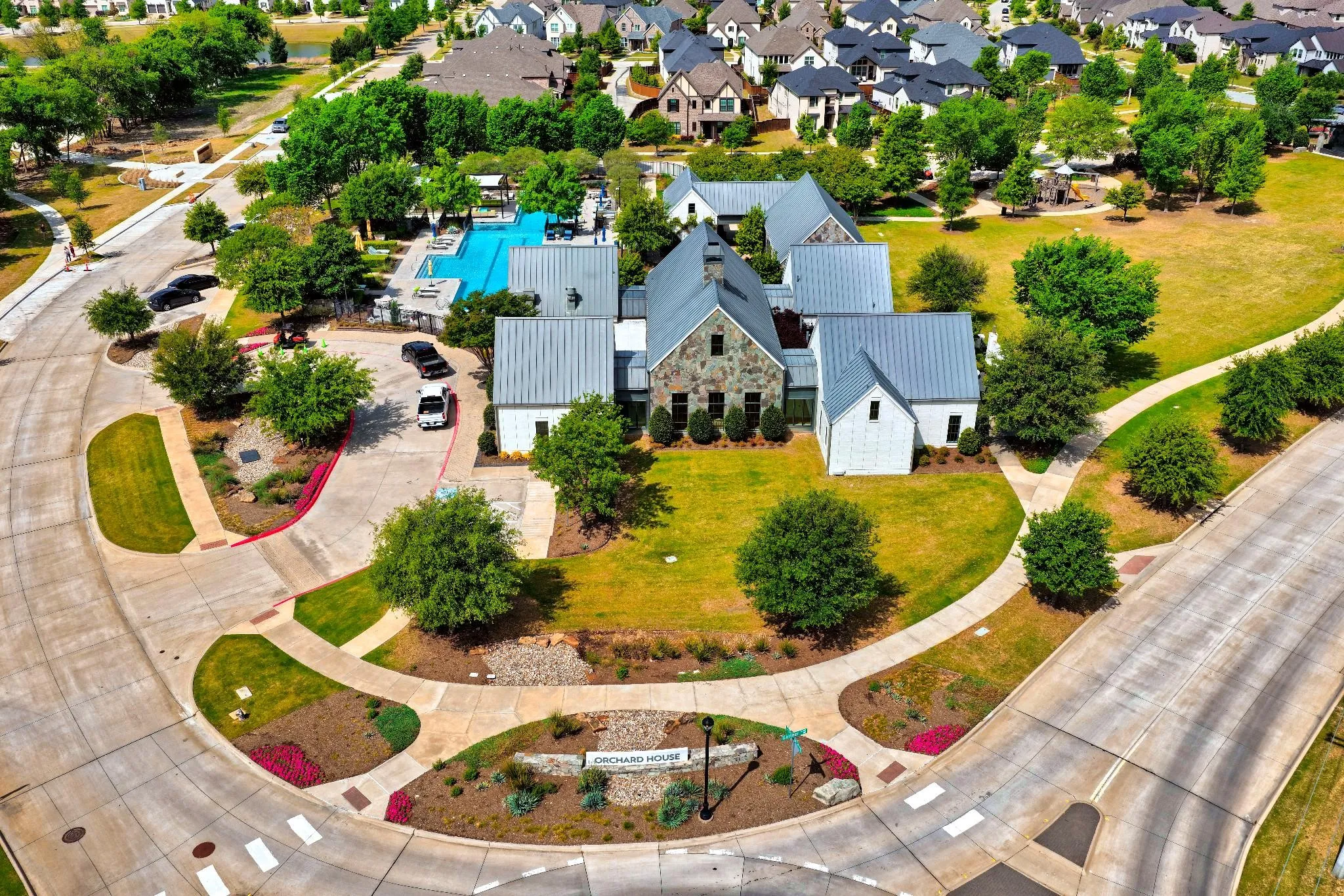 Community amenity center featuring a multi-building clubhouse with stone and vertical siding exteriors, a large outdoor swimming pool, and dedicated parking
