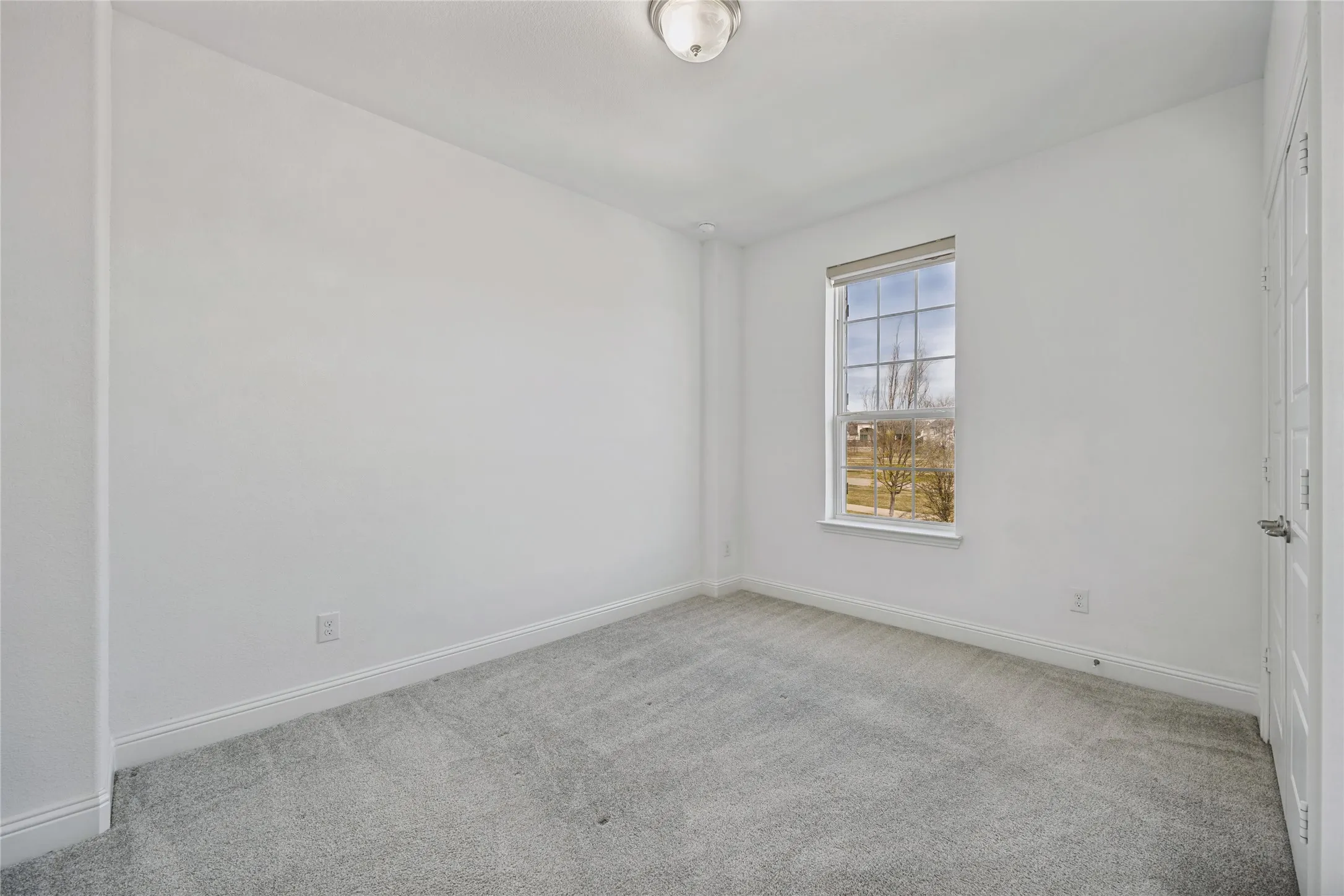 Bright room featuring light grey carpeting, white walls, a single window, a flush mount ceiling light, and white trim