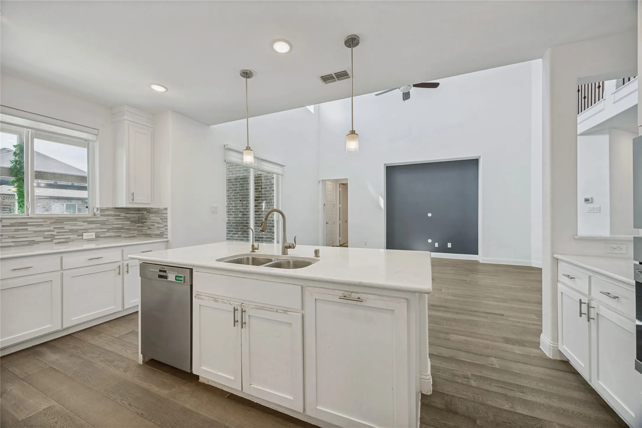 Contemporary kitchen featuring a large central island with a double sink, white cabinetry, a built-in dishwasher, and wood-finish flooring