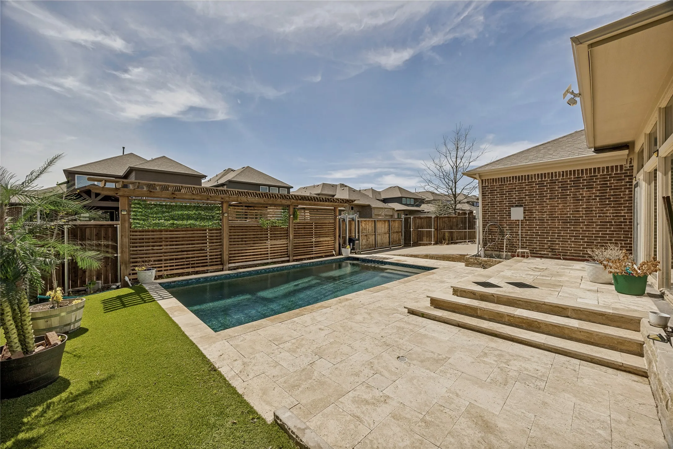 Outdoor living space featuring a rectangular swimming pool with stone coping, a large stone patio, and a wood pergola structure