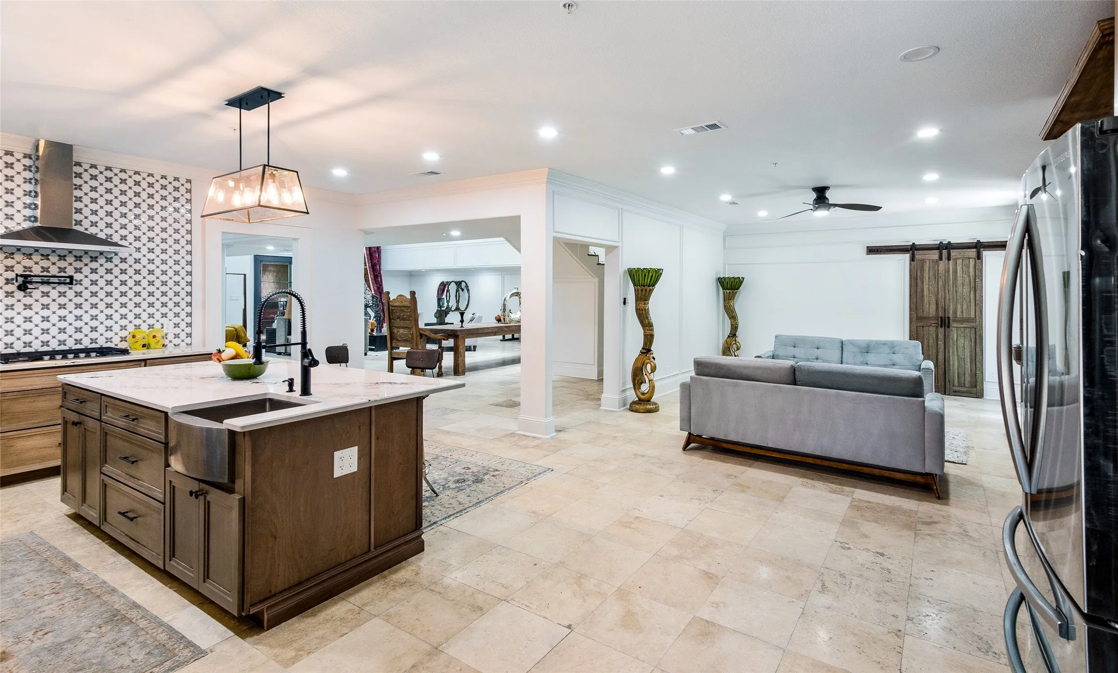 Kitchen featuring a barn door, stainless steel appliances, light stone countertops, an island with sink, and hanging light fixtures