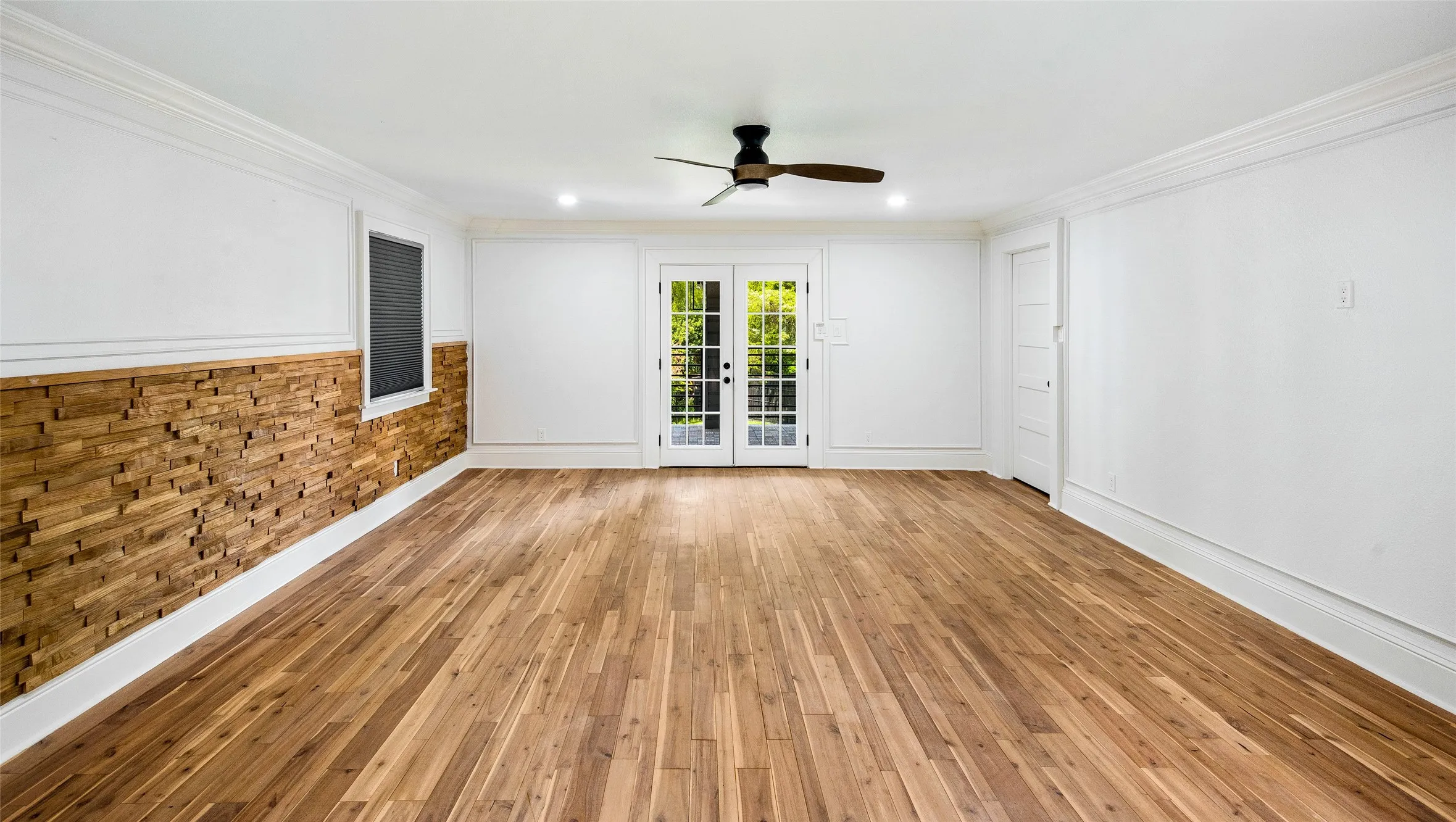 Spare room with light wood-type flooring, a ceiling fan, ornamental molding, french doors, and wooden walls