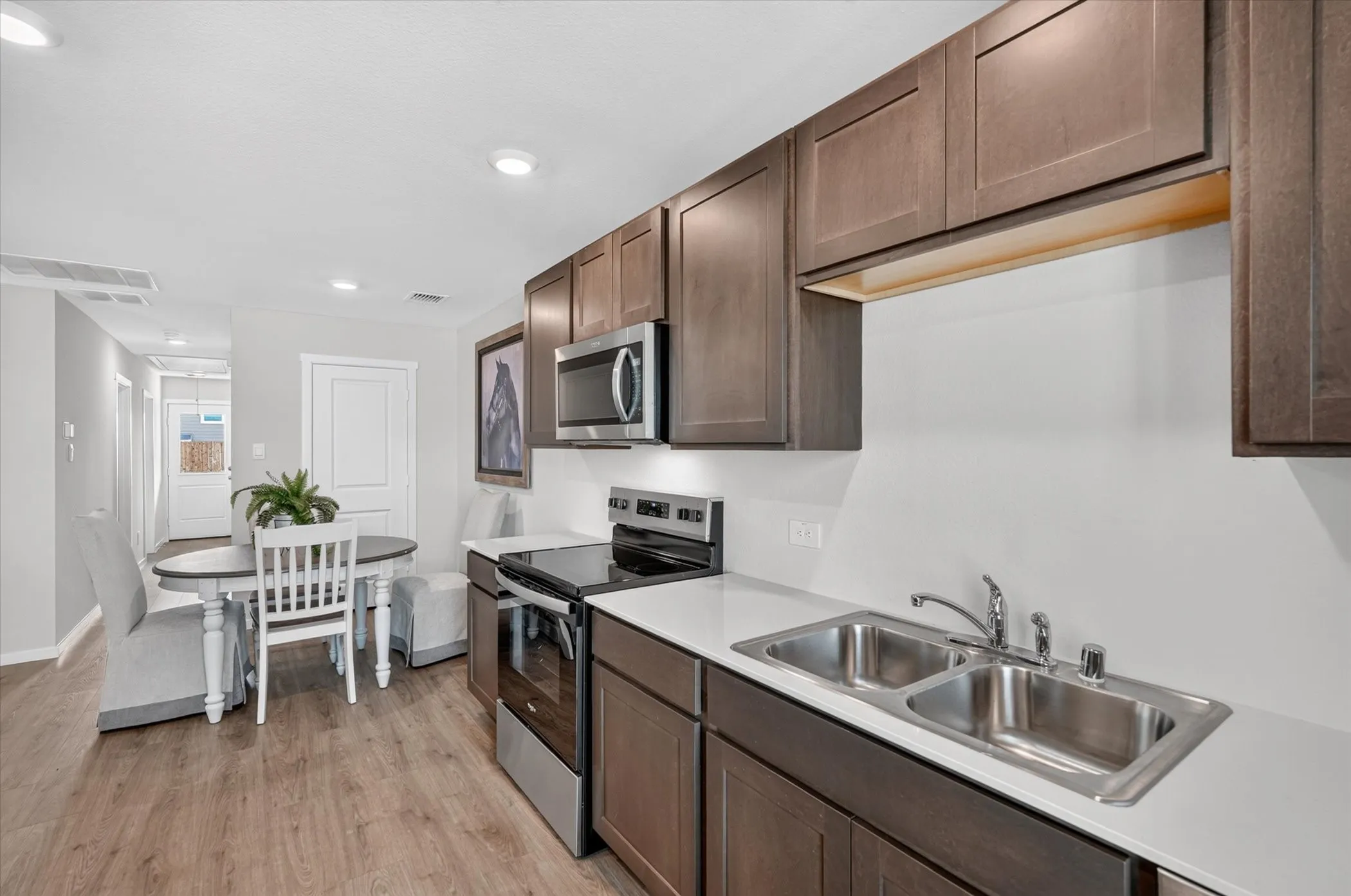 Stainless steel appliances, wood-finish flooring, recessed lighting, white countertops, and dark wood-finish cabinetry