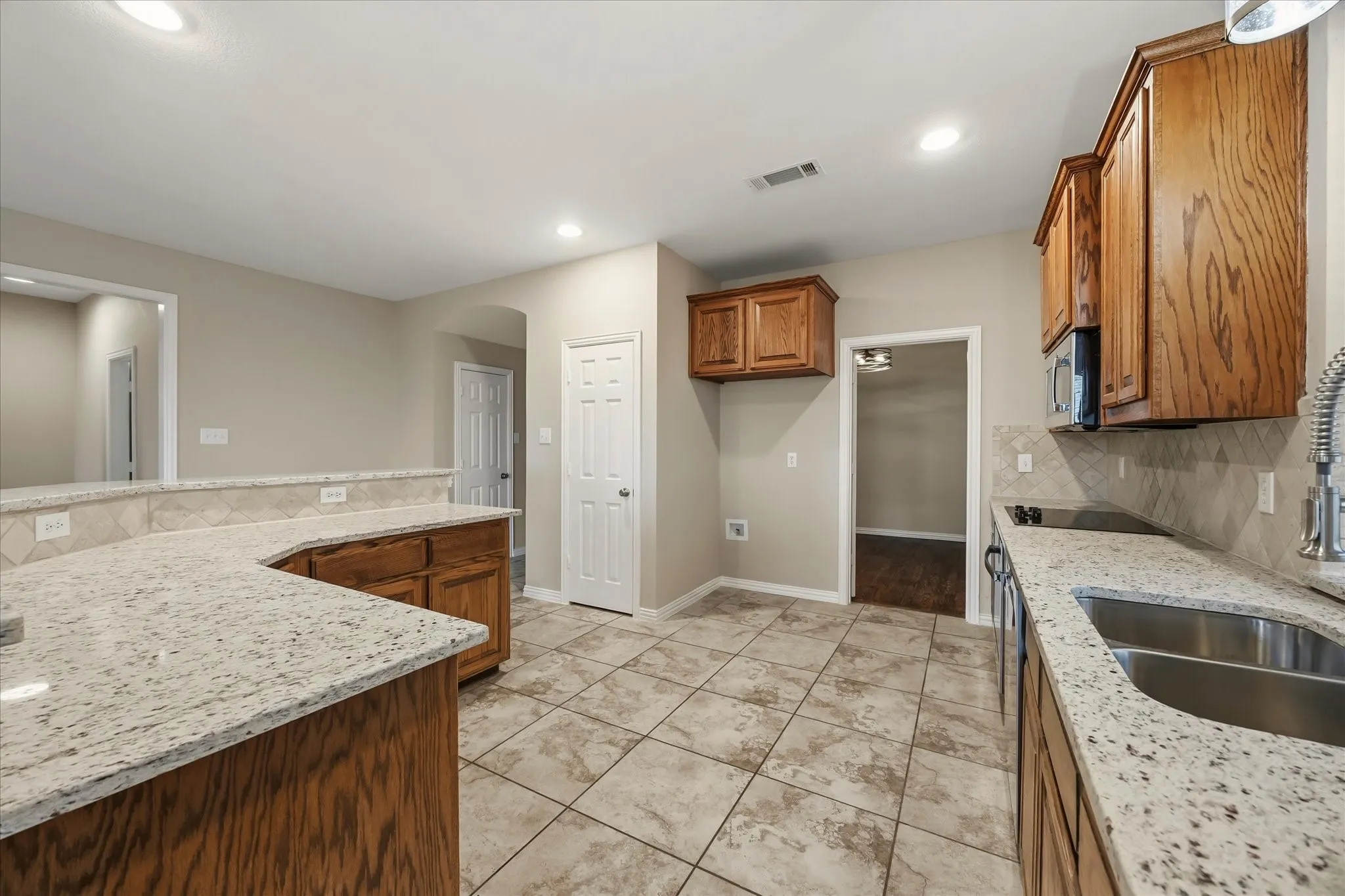 Kitchen featuring tile flooring, granite countertops, wood cabinetry, stainless steel sink, and tile backsplash