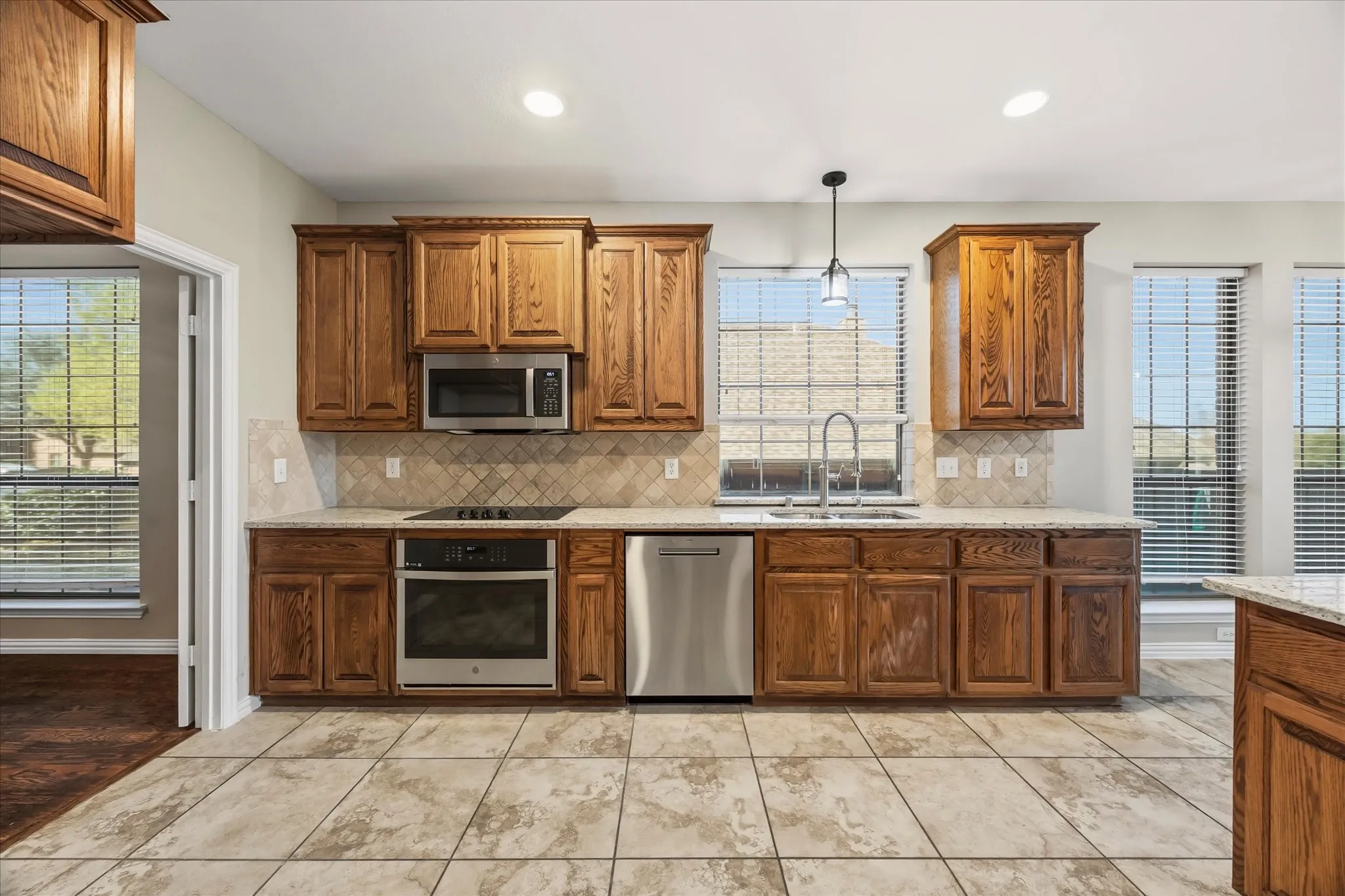 Kitchen featuring wood cabinetry, stainless steel appliances, a tile backsplash, and a large sink with a gooseneck faucet