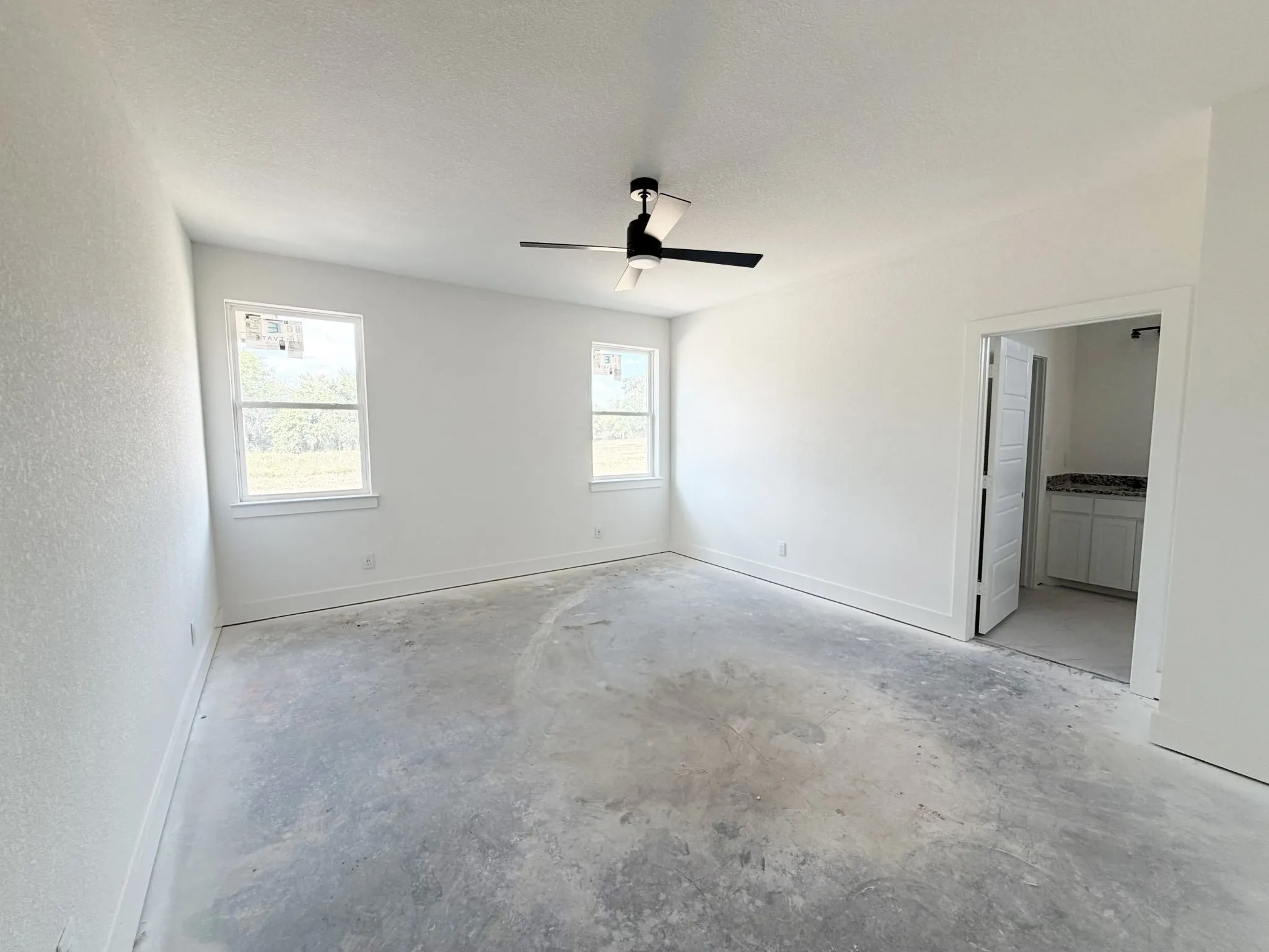 Spacious room with white walls, two windows, and a ceiling fan with black blades