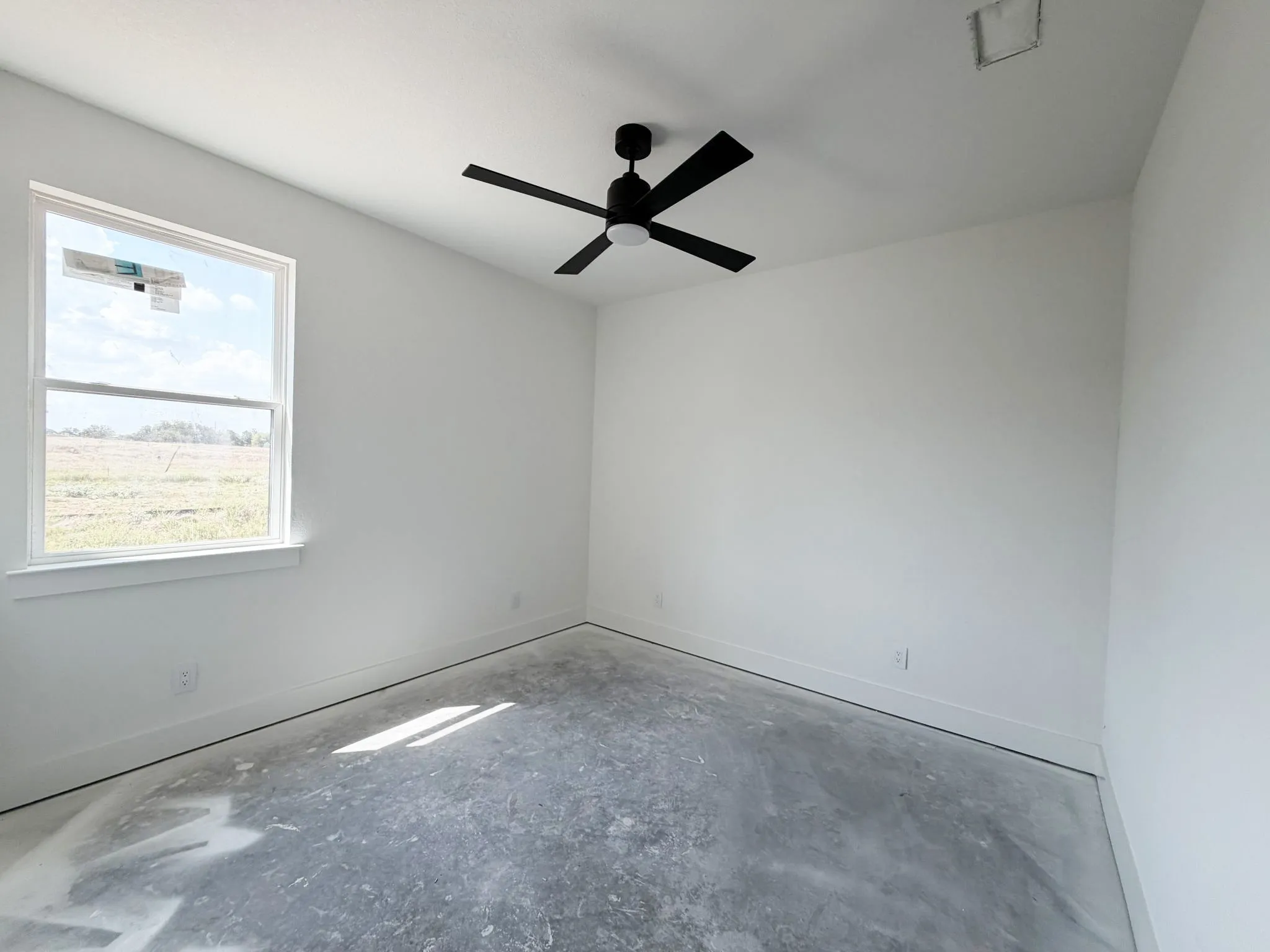 White walls with a ceiling-mounted fan, large window, and concrete flooring
