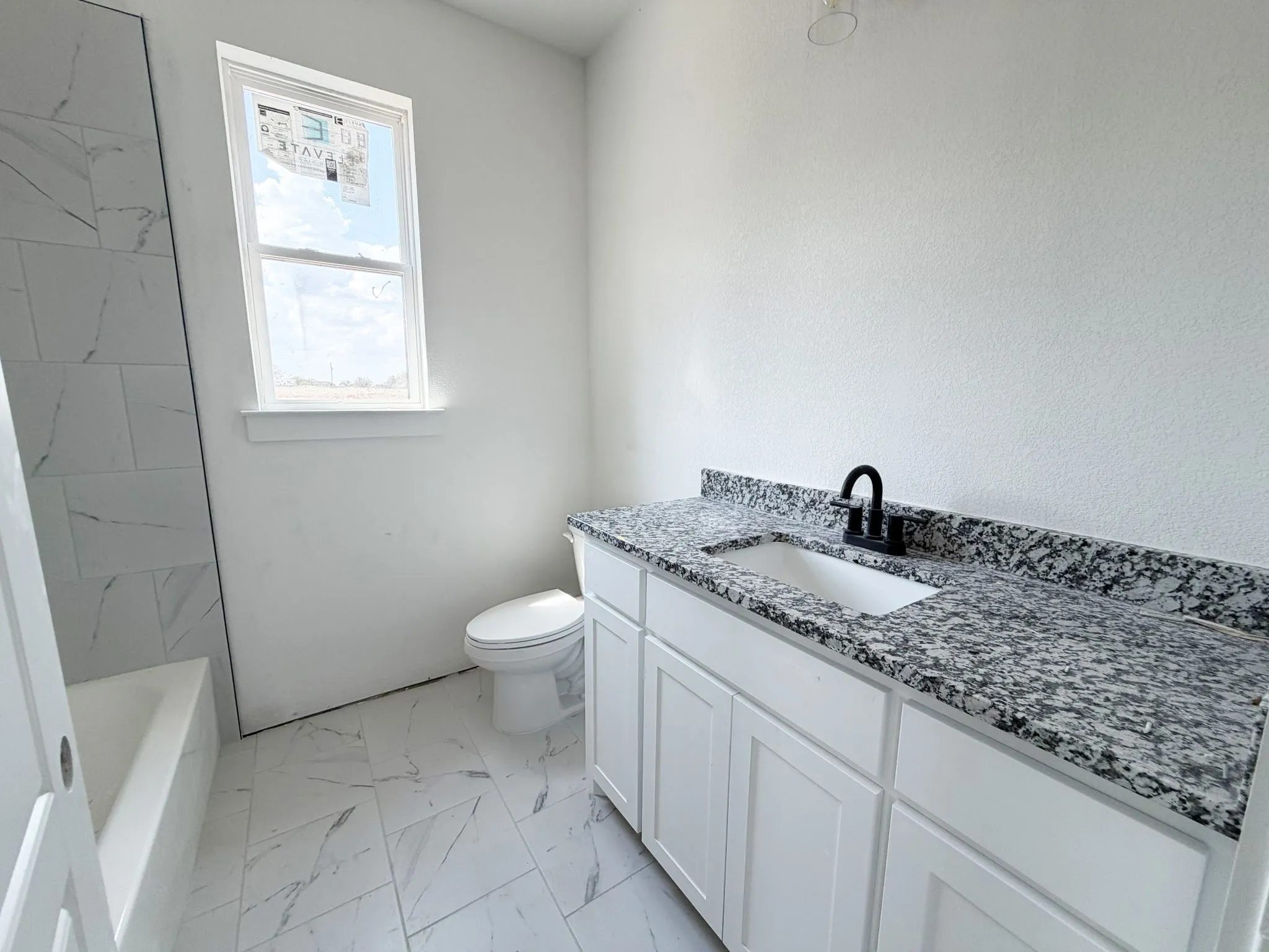 White shaker-style vanity with a speckled countertop, undermount sink, and matte black faucet