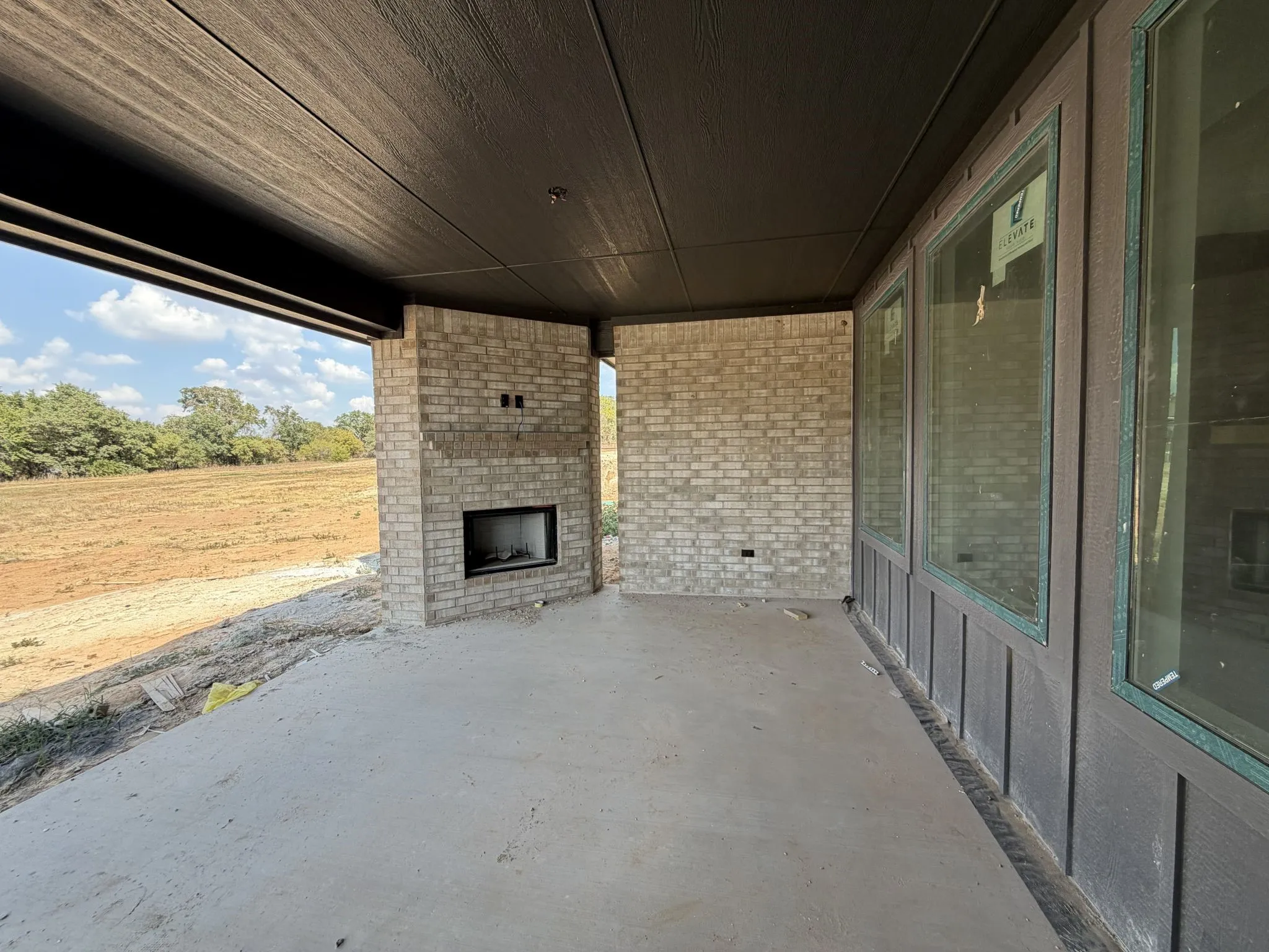 Expansive outdoor living area featuring a built-in fireplace, concrete flooring, large windows, and a dark wood-finish ceiling