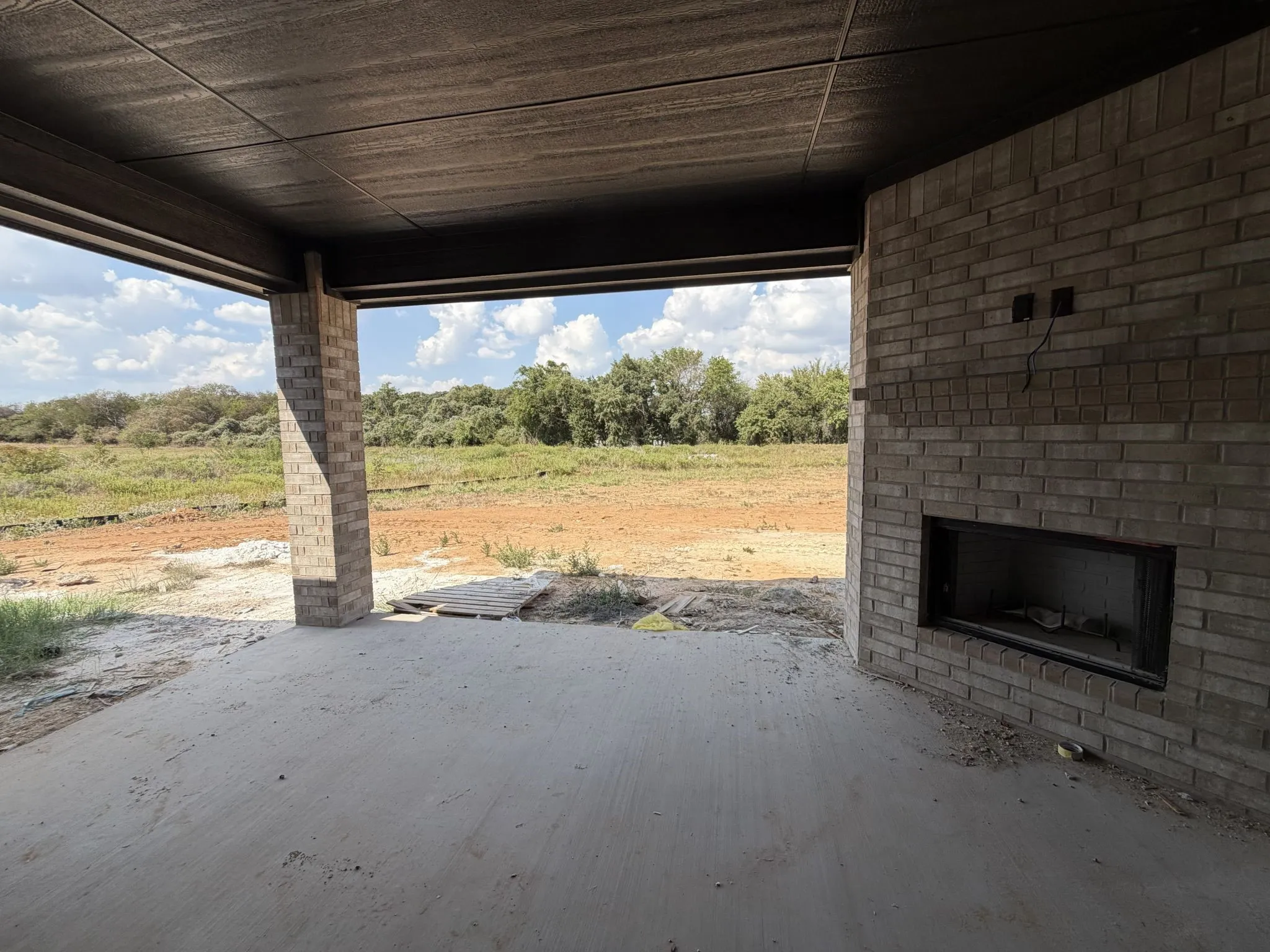 Covered outdoor living space featuring a brick fireplace, concrete flooring, and brick columns