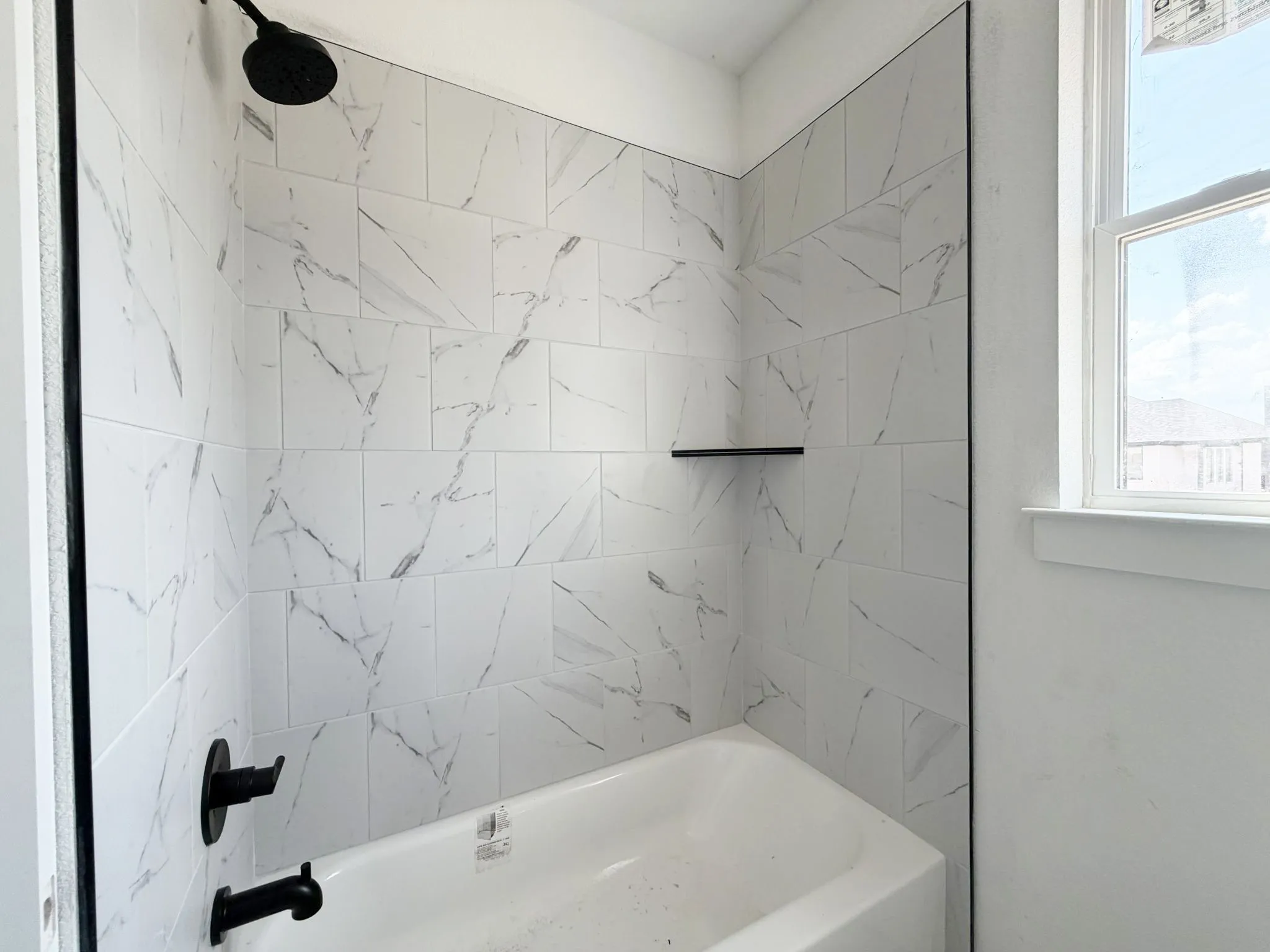 Bathtub and shower combination with white tile surround, a built-in shower shelf, and matte black fixtures
