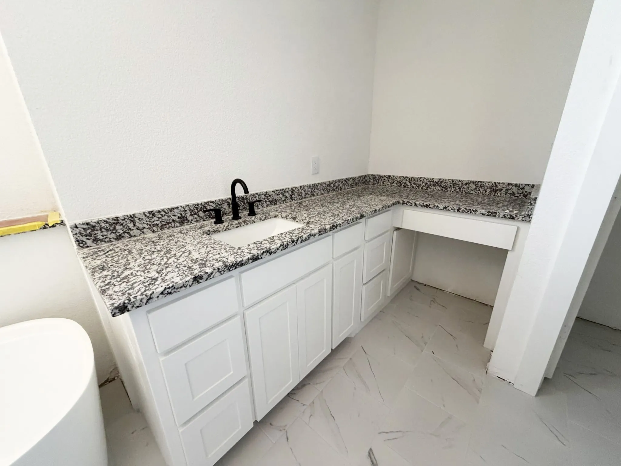 White shaker-style cabinetry with an integrated sink, black faucet, and patterned countertop