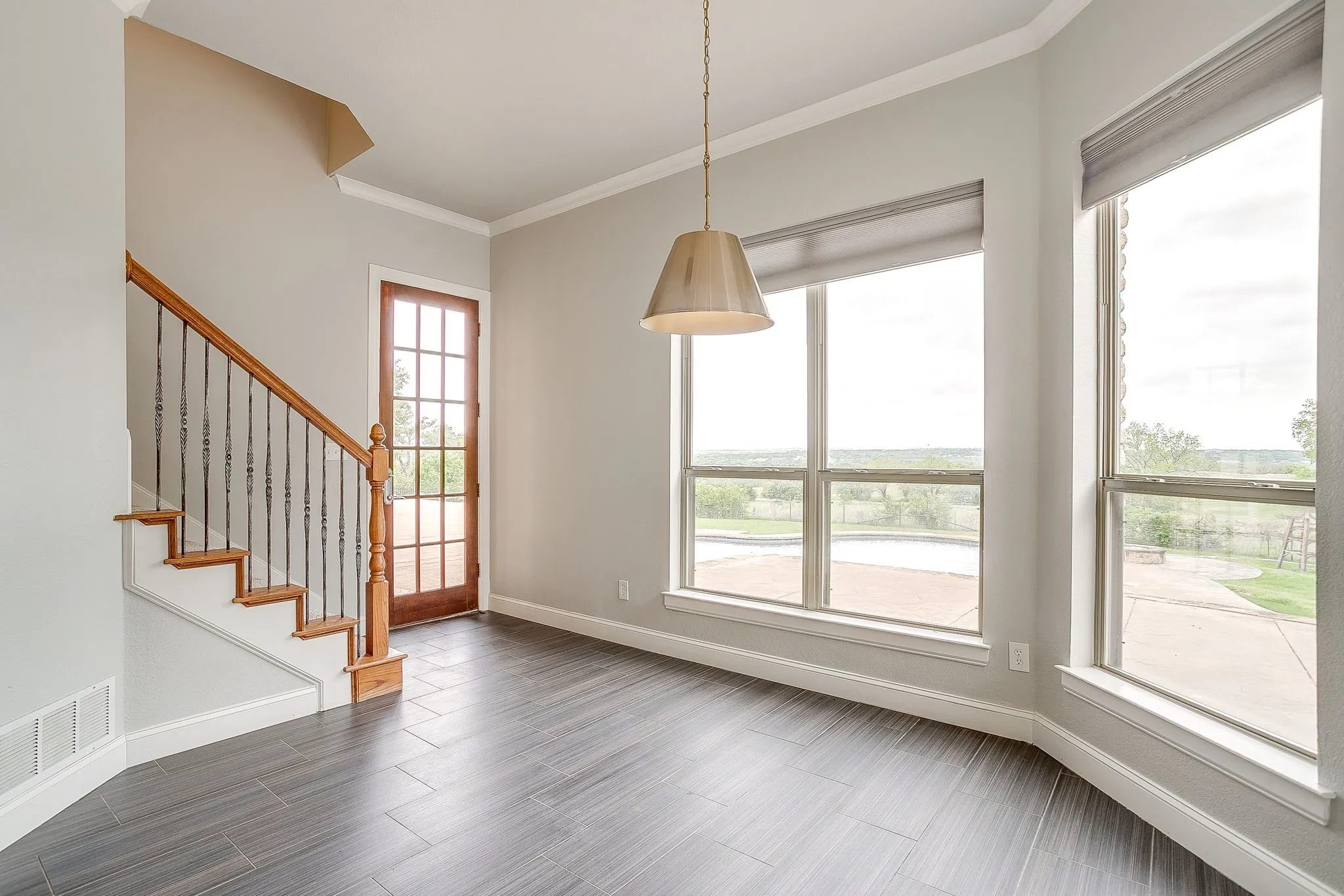 Entryway featuring dark tile flooring, a wooden staircase with wrought iron balusters, a glass-paneled door, and large windows with roller shades