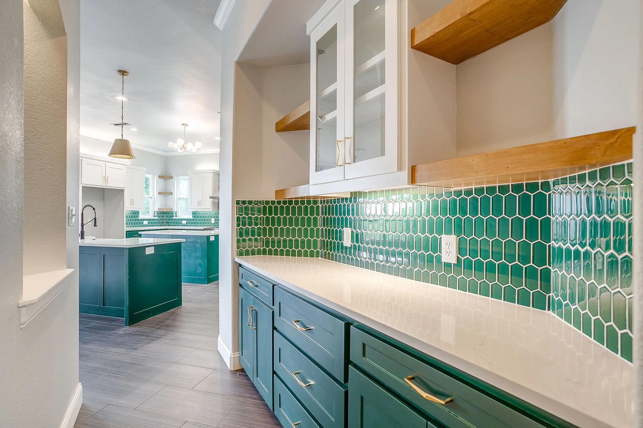 Kitchen area featuring a deep green tiled backsplash, white countertops, and white upper cabinetry with glass inserts
