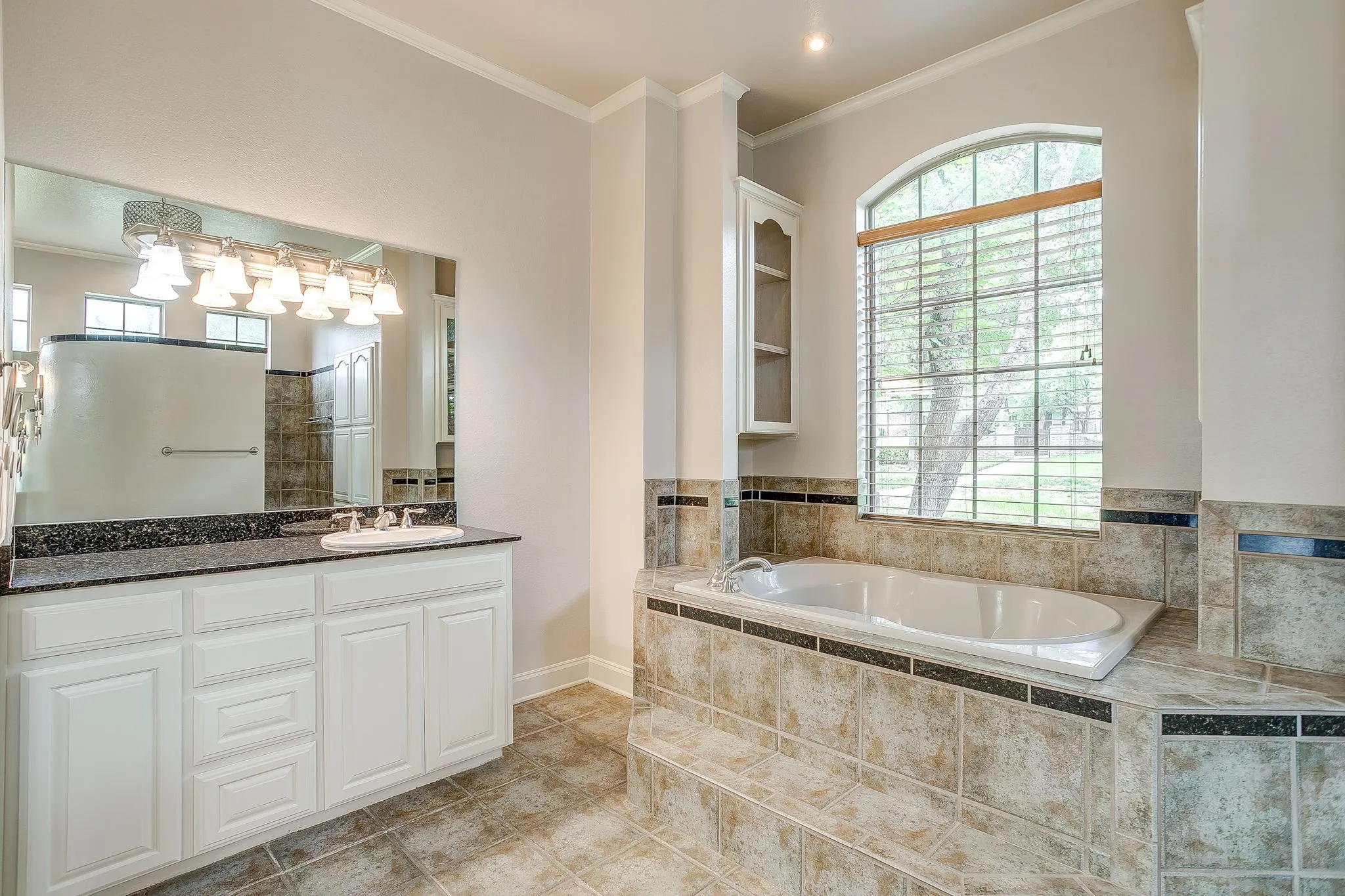 Bathroom featuring a tiled floor, a vanity with a dark countertop and white cabinetry, a bathtub encased in tile, and an arched window
