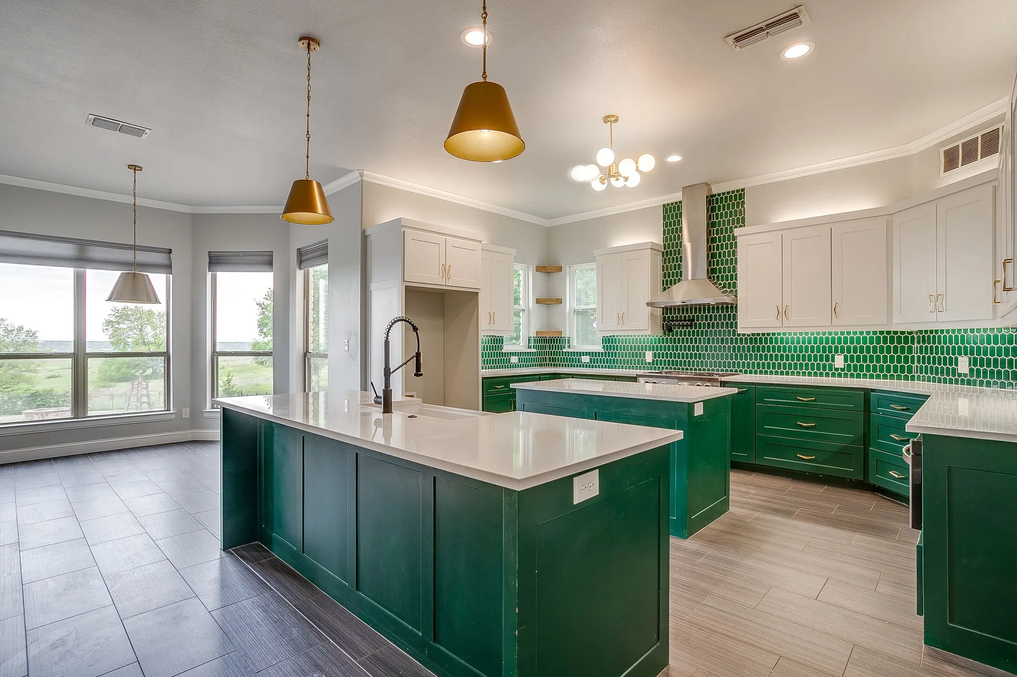 The kitchen features two islands with white countertops, green cabinetry, and a green tiled backsplash