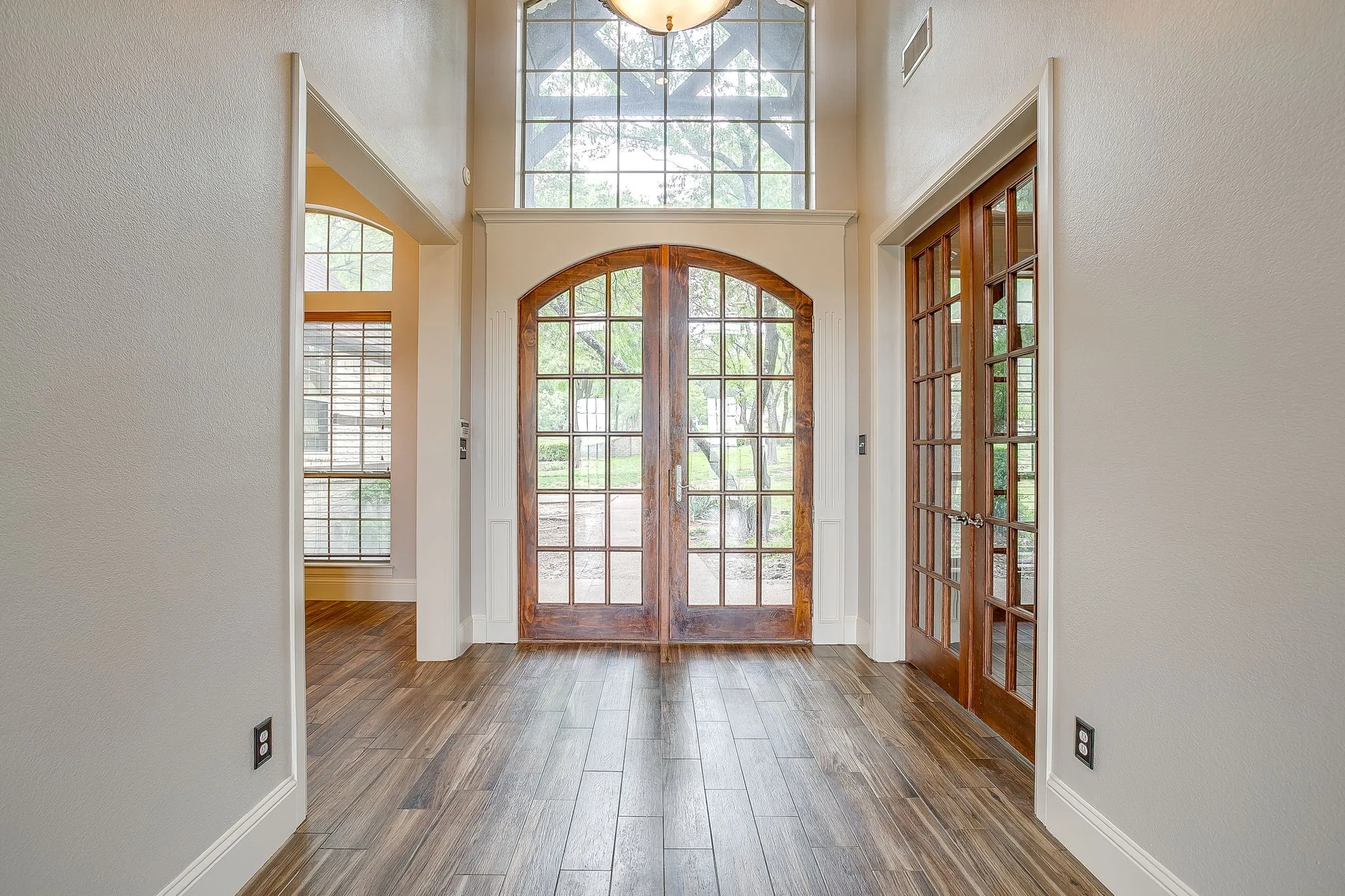 Entryway featuring wood-look flooring, arched double doors with glass panels, and a prominent window above