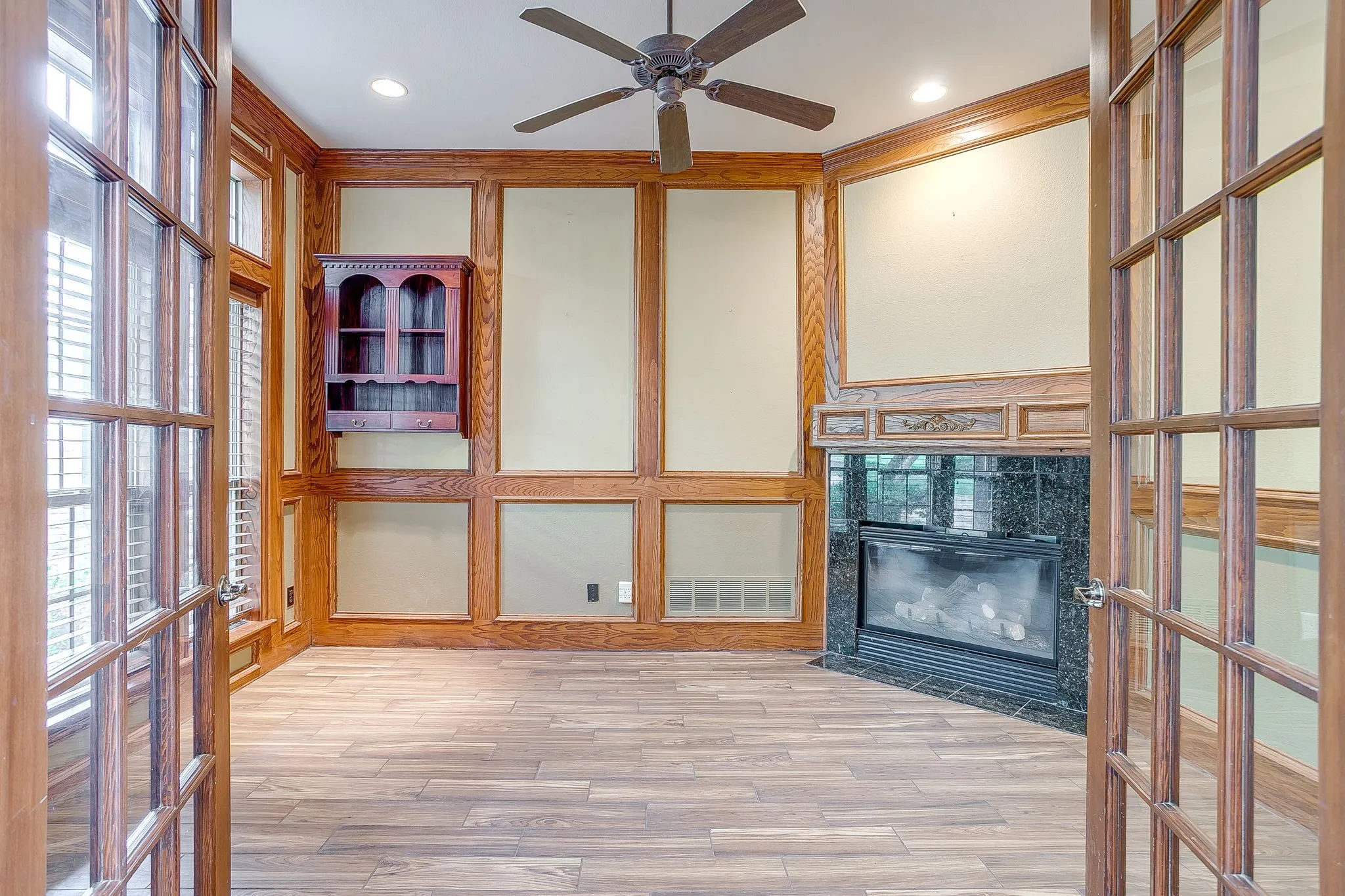This versatile room features wood flooring, a fireplace with a black marble surround, and wood paneled walls