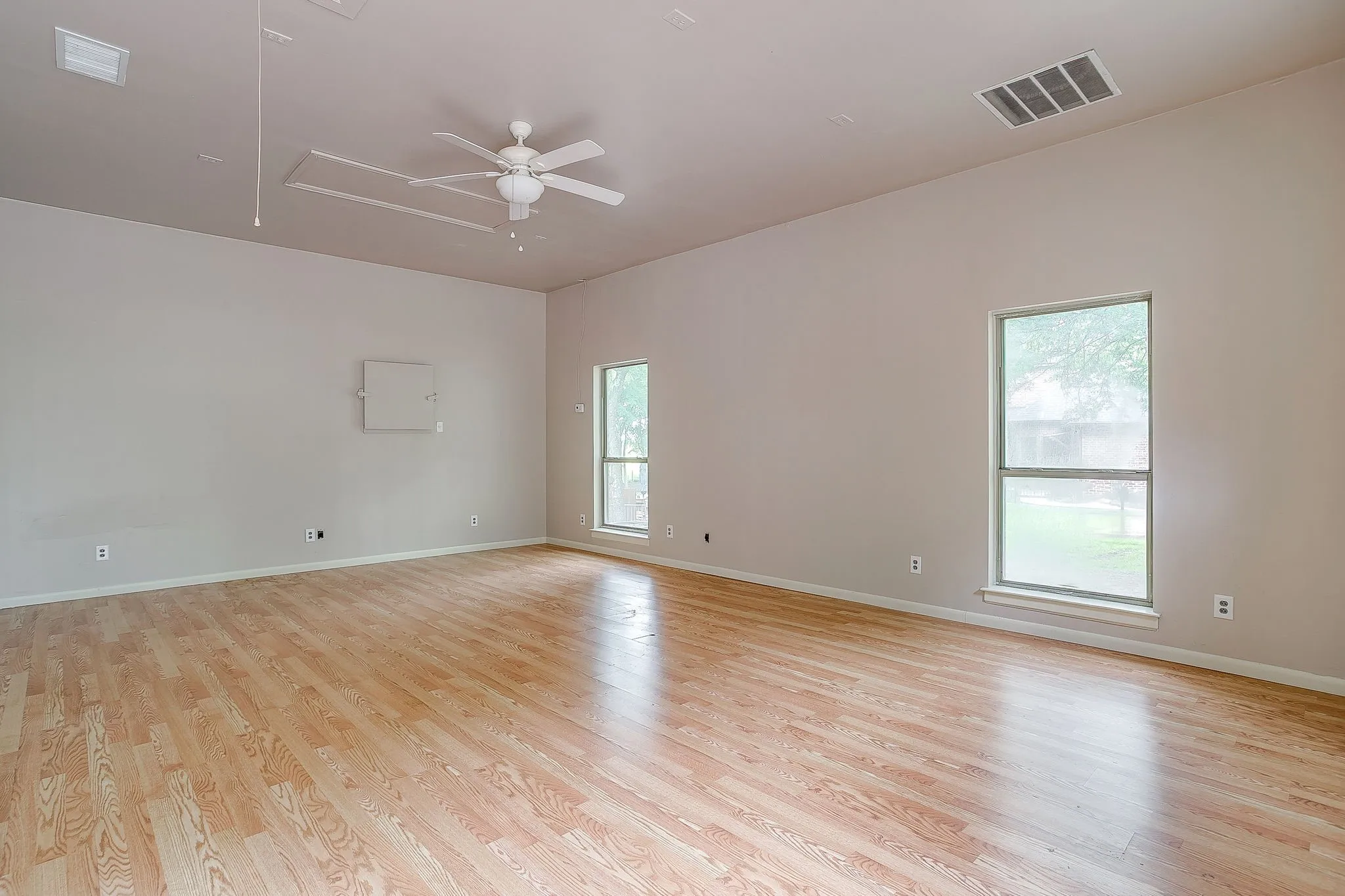 Spacious room featuring light wood flooring, neutral tone walls, and two windows providing natural light