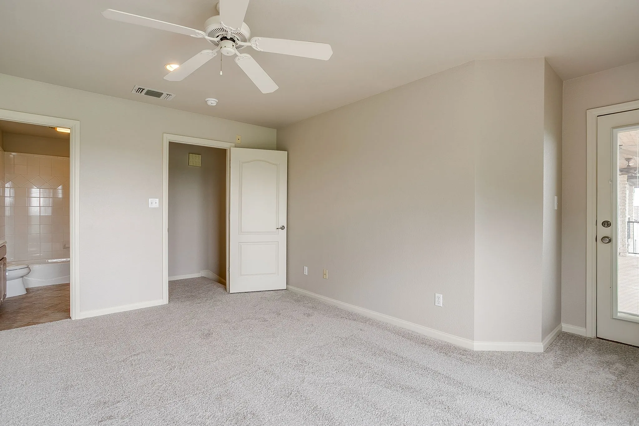 This bright room features neutral-toned walls, light grey carpeting, and a ceiling fan