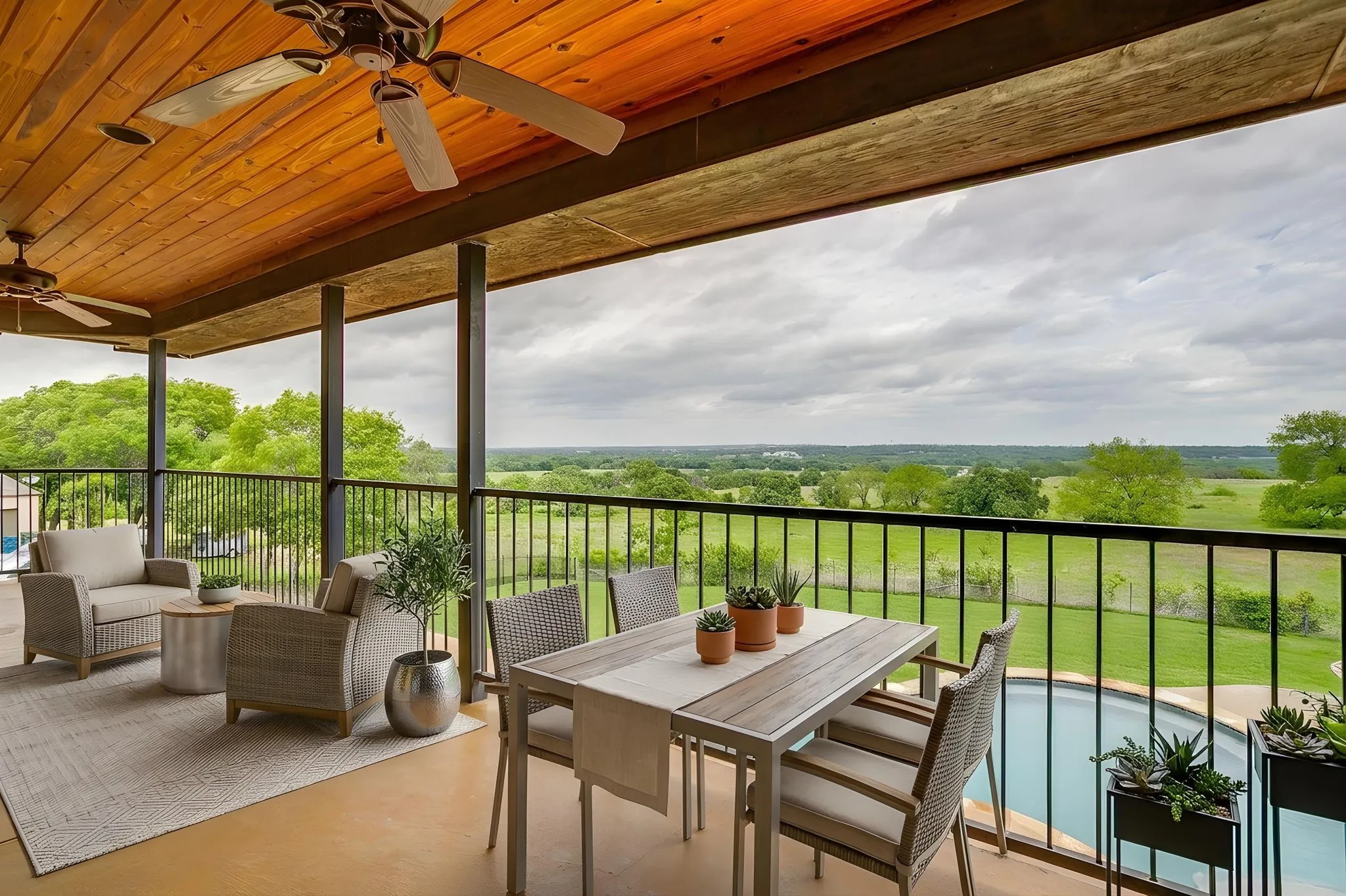 Expansive covered patio featuring a wood-paneled ceiling with ceiling fans, offering views of the surrounding green landscape and a pool