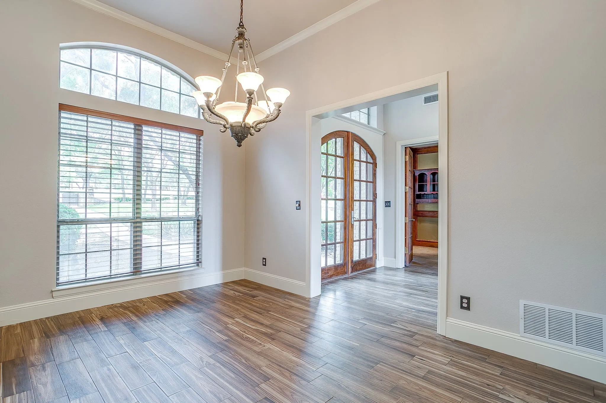 This room features wood-look tile flooring, a large window with an arched transom, and a decorative chandelier