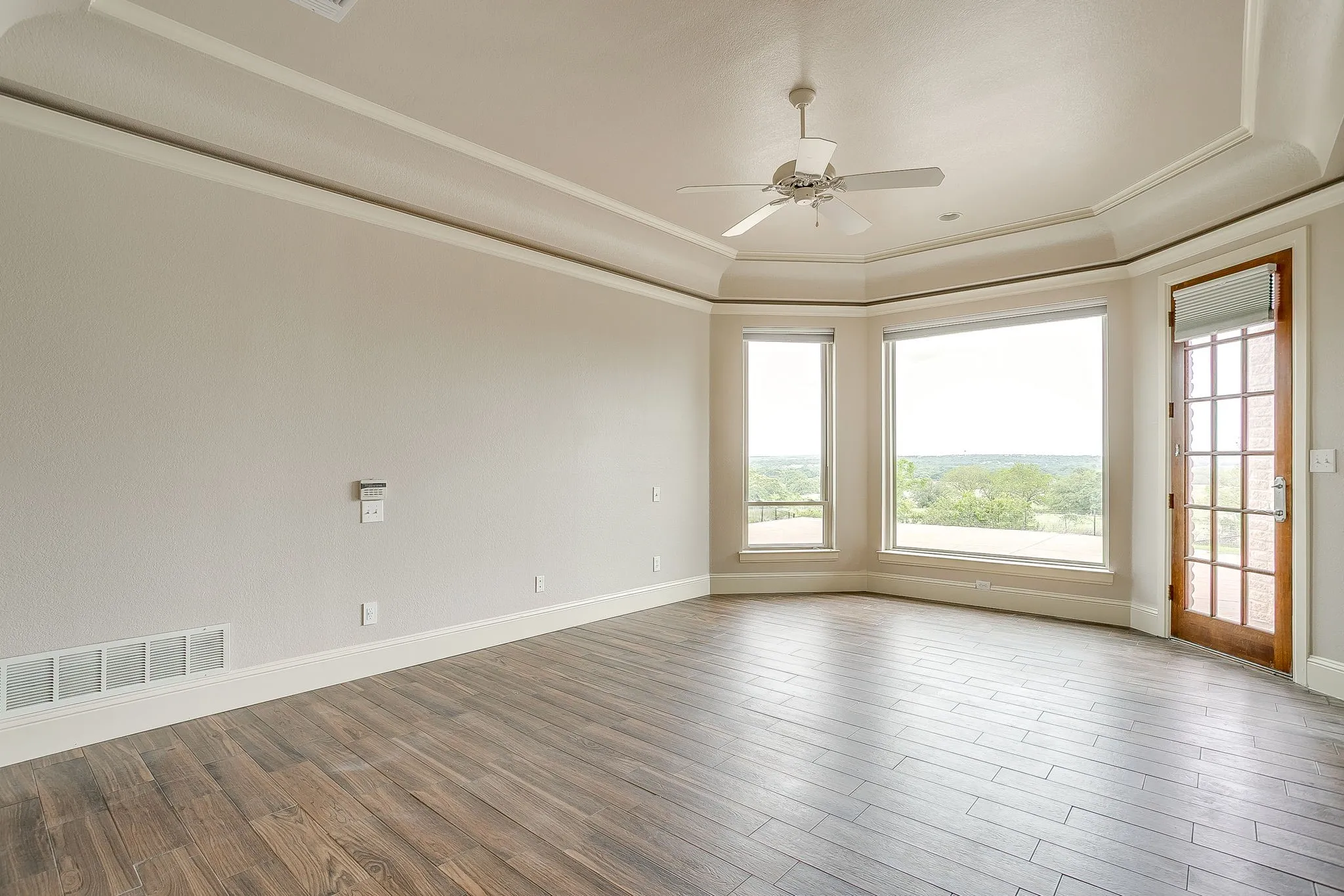 This room features wood-look flooring, a tray ceiling with crown molding, and a ceiling fan