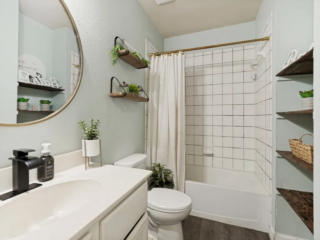 Bathroom featuring a white vanity with an integrated sink and matte black faucet, a round wall mirror, a toilet, a shower-over-tub combination