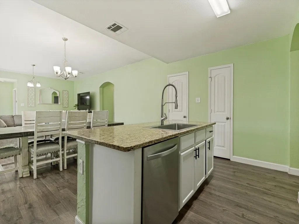 Kitchen island featuring a stainless steel sink with a high-arch faucet, a dishwasher, and stone-finish countertops