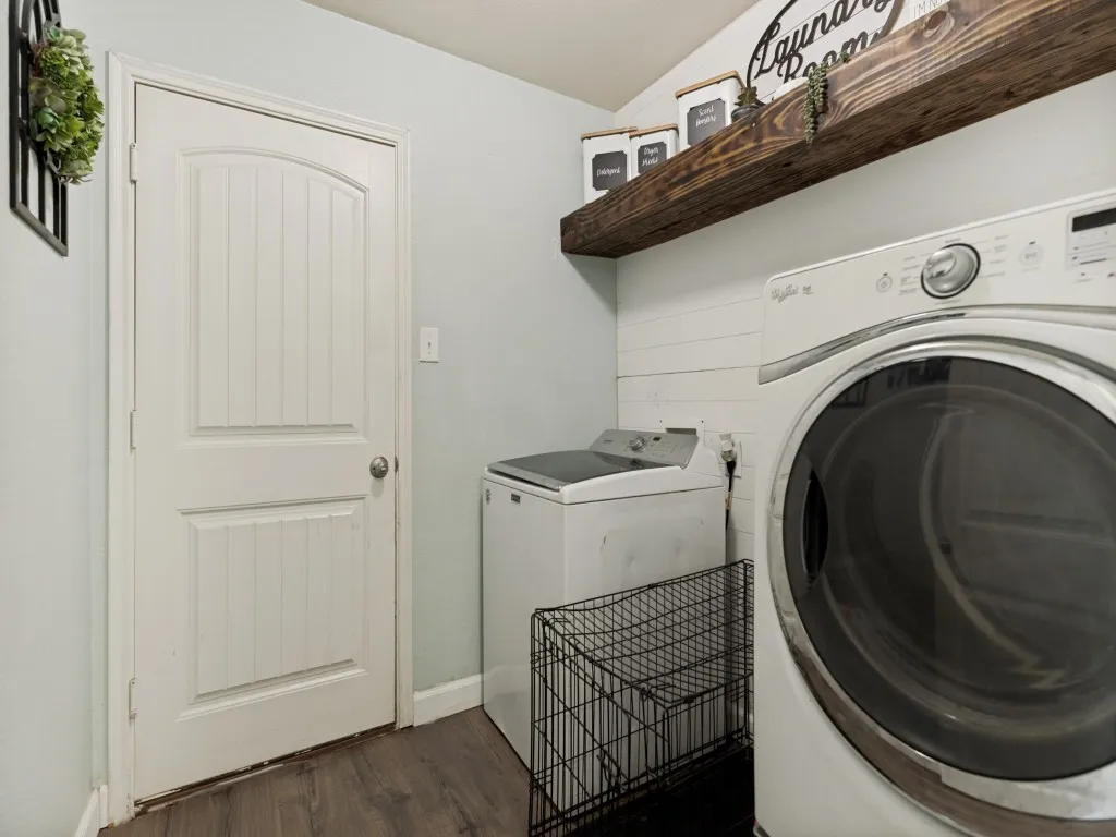 Dedicated laundry area featuring full size hook-up and a rustic wood floating shelf over a shiplap accent wall.  This is also the access to and from the garage.
