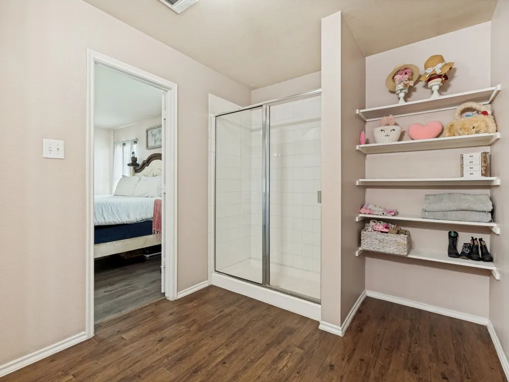 Unwind in the spacious primary bath, featuring a large walk-in shower and open shelving for convenient storage and organization.