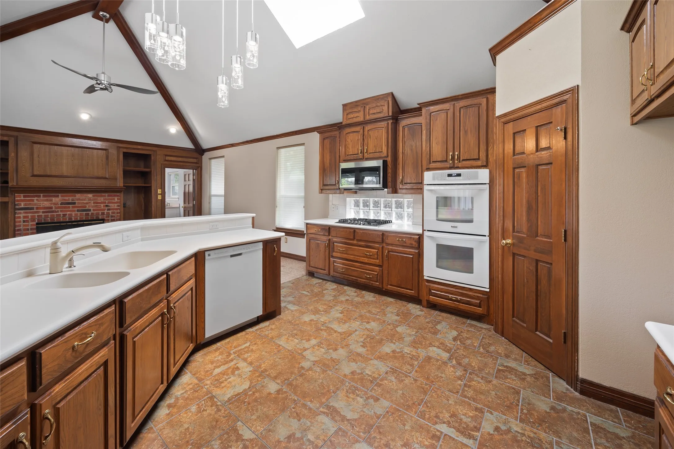 Kitchen featuring ceiling fan, light countertops, white appliances, light stone finish flooring, and wood finish cabinets