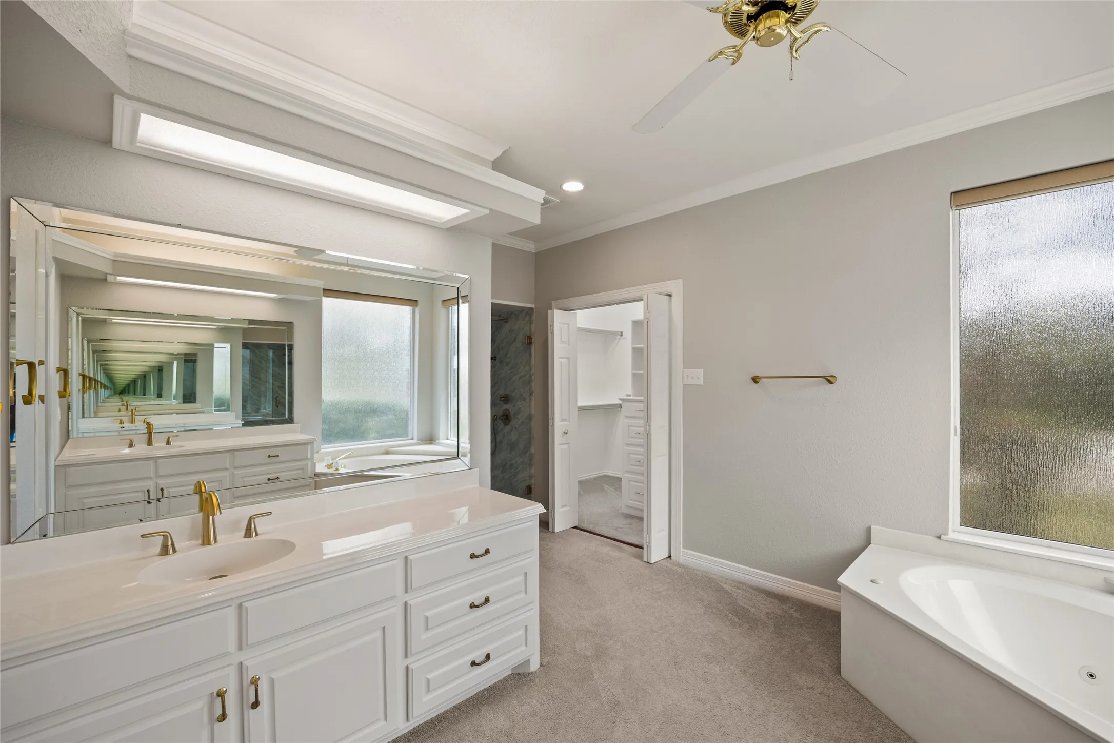 Bathroom with a bath, vanity, crown molding, a walk in closet, and light colored carpet
