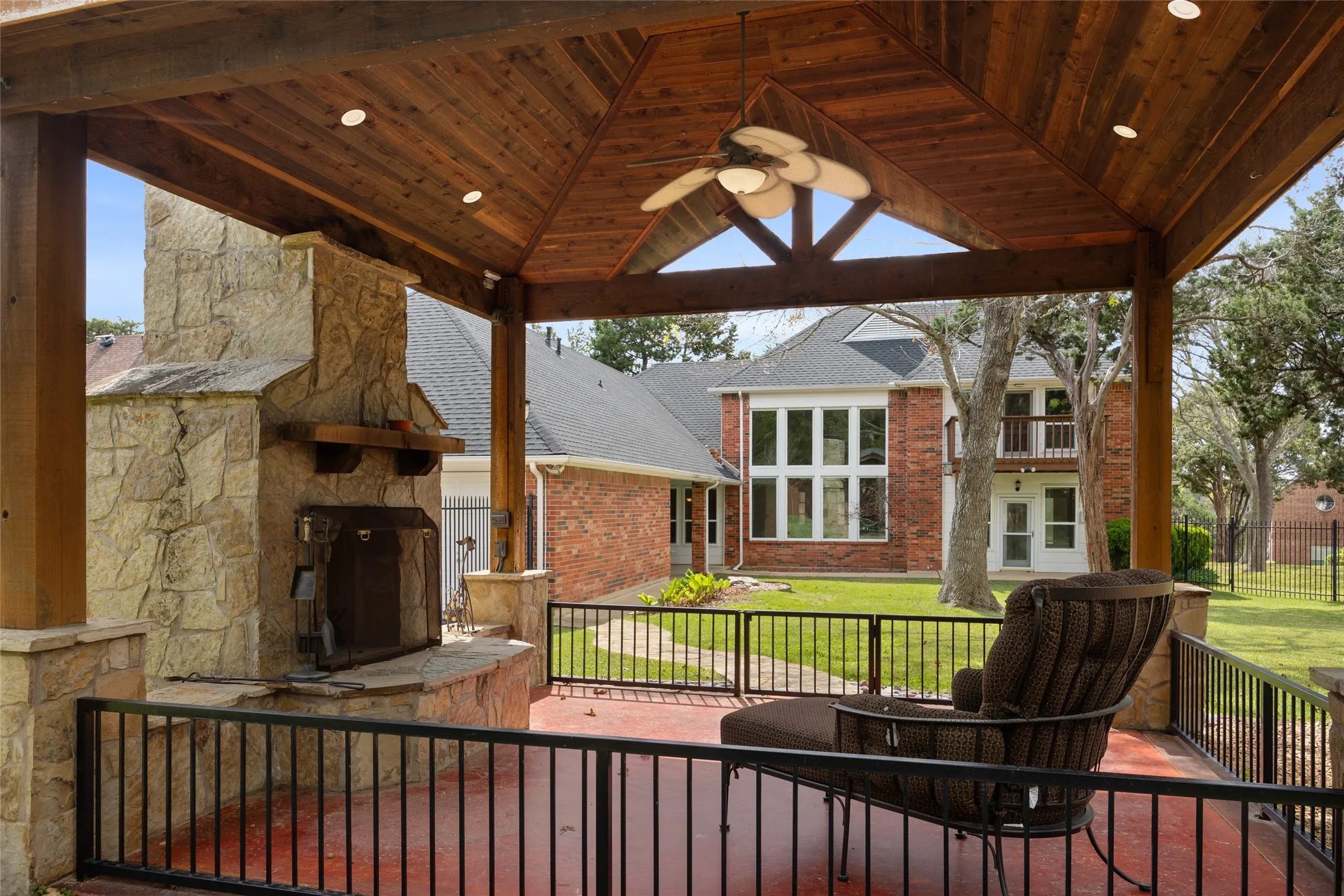 Large covered patio with an outdoor stone fireplace, ceiling fan, and a large expansive yard for pool addition or your pets to roam free.