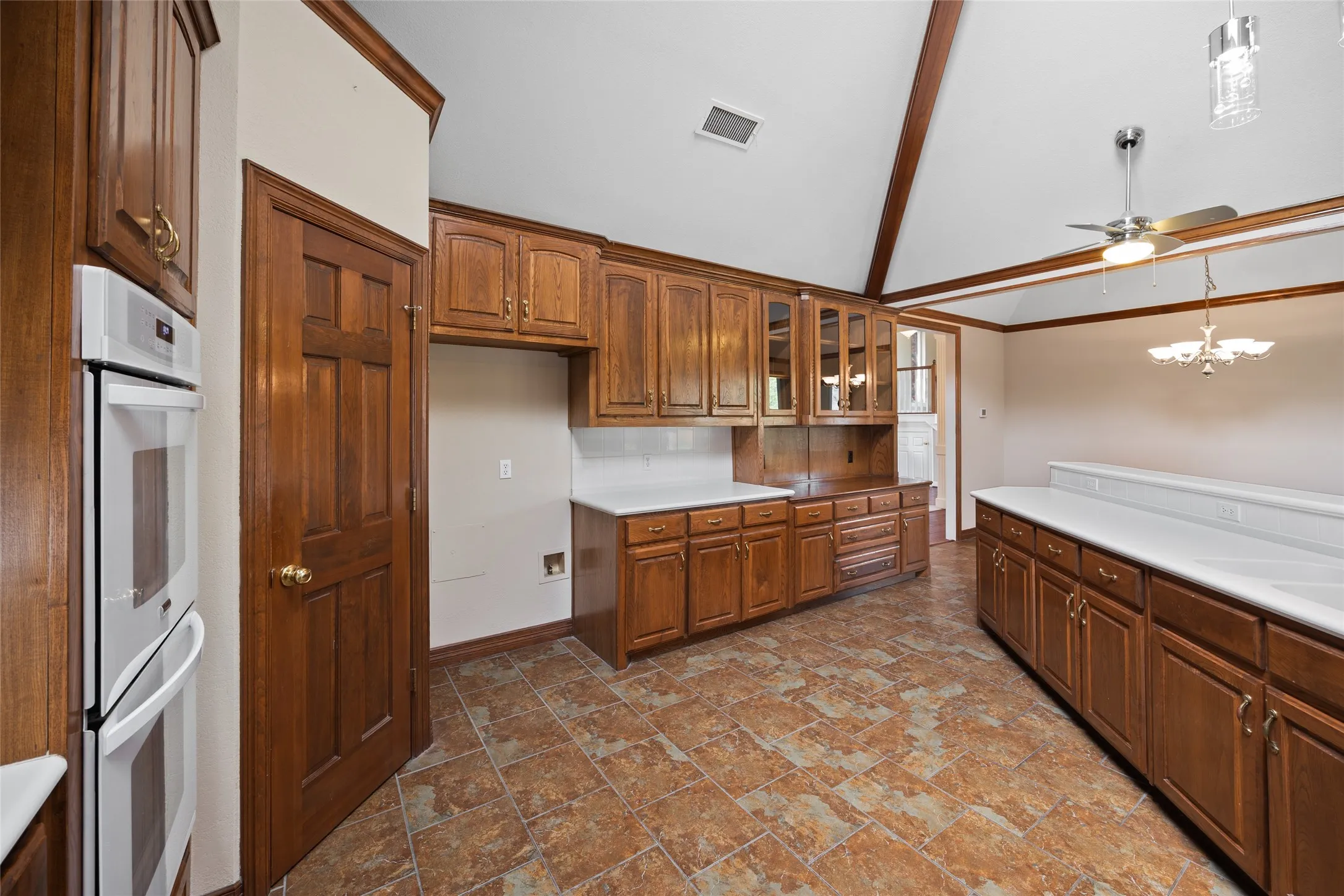 Kitchen with pendant lighting, glass fronted cabinets, ceiling fan, double oven, and lofted ceiling
