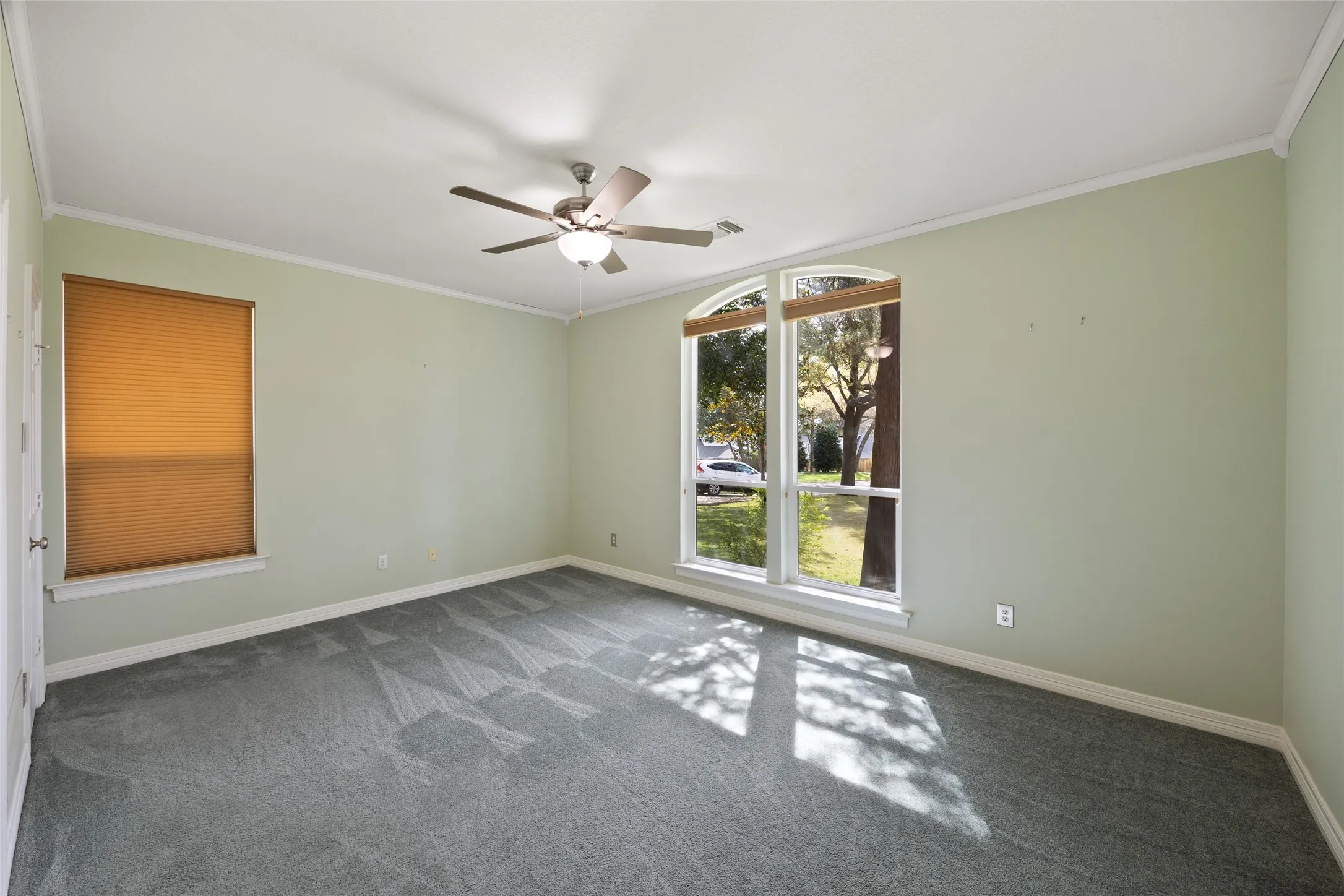 Unfurnished bedroom on first floor  featuring dark carpet, ornamental molding, and a ceiling fan front of home.