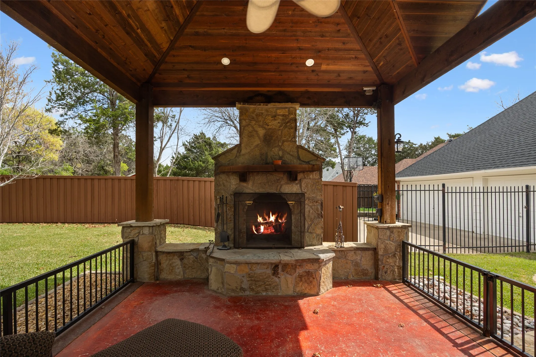 Fenced backyard featuring an outdoor stone fireplace, a patio area, and ceiling fan