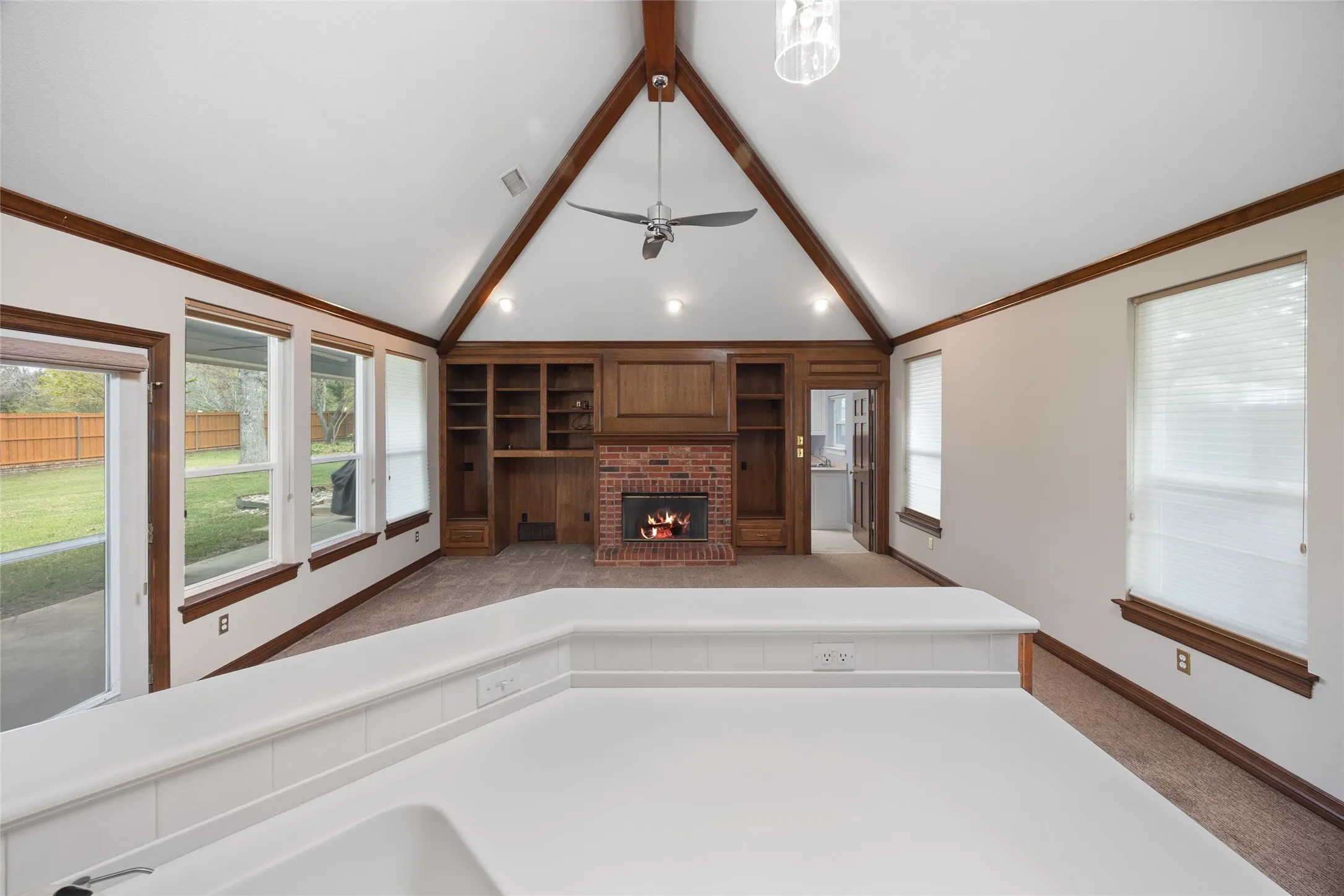 Unfurnished living room featuring dark carpet, built in features, beamed ceiling, a fireplace, and a ceiling fan